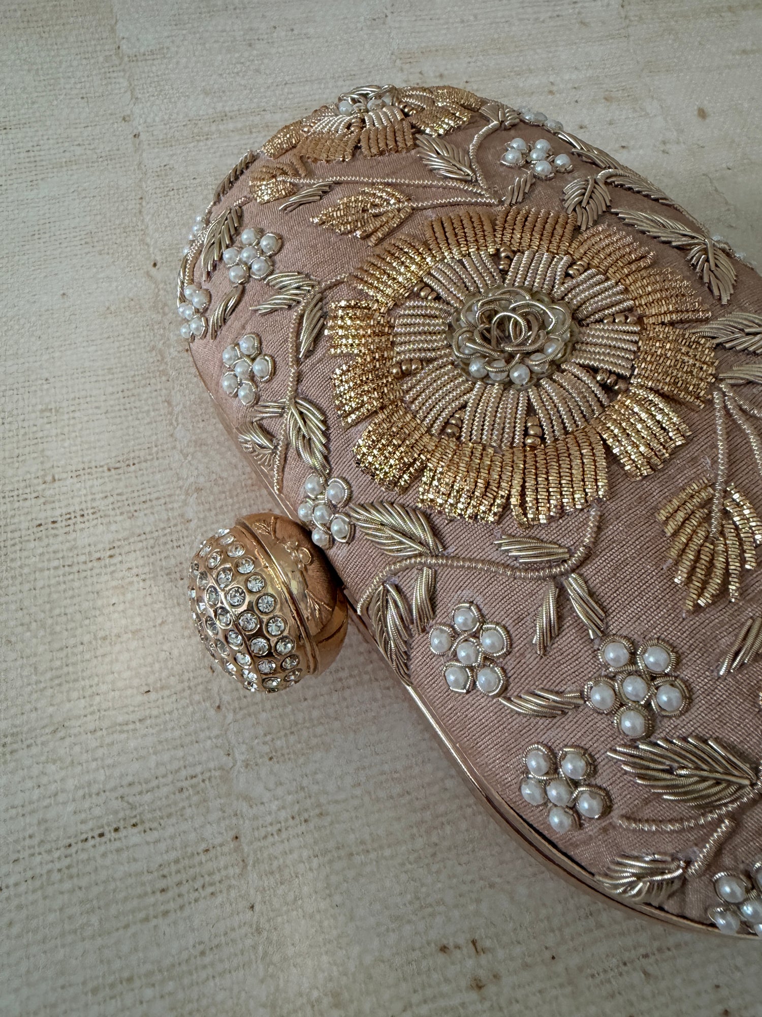 Decorative clutch with gold embroidery and pearl embellishments on a textured beige background