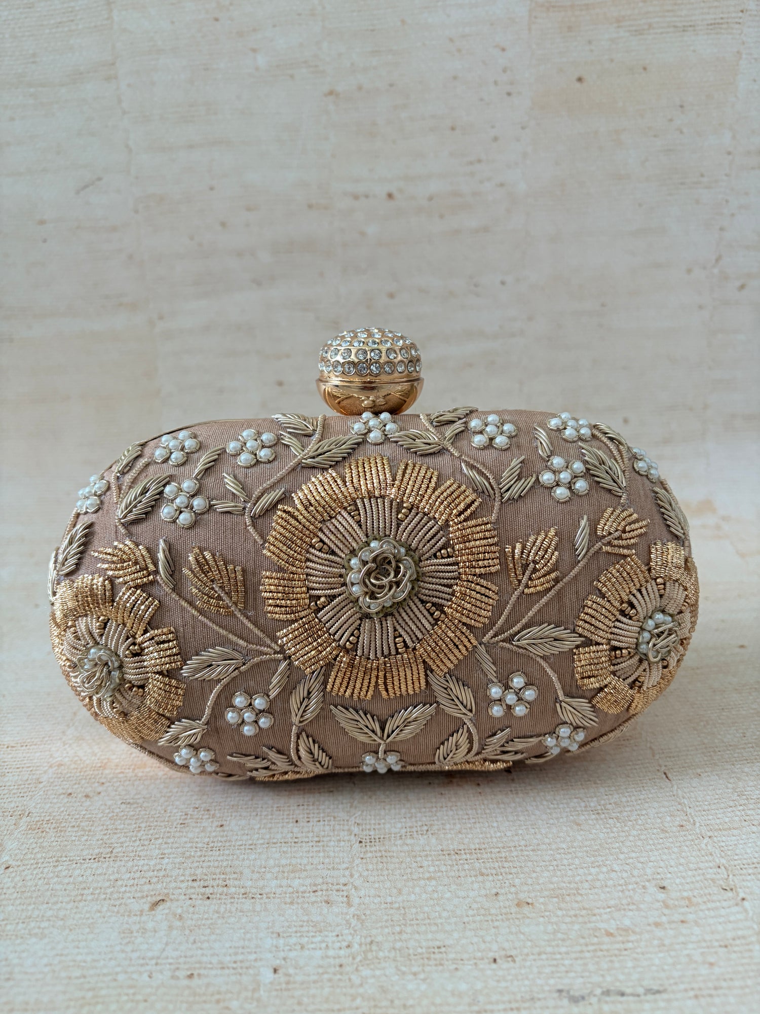 Decorative clutch bag with floral embroidery on a textured beige background