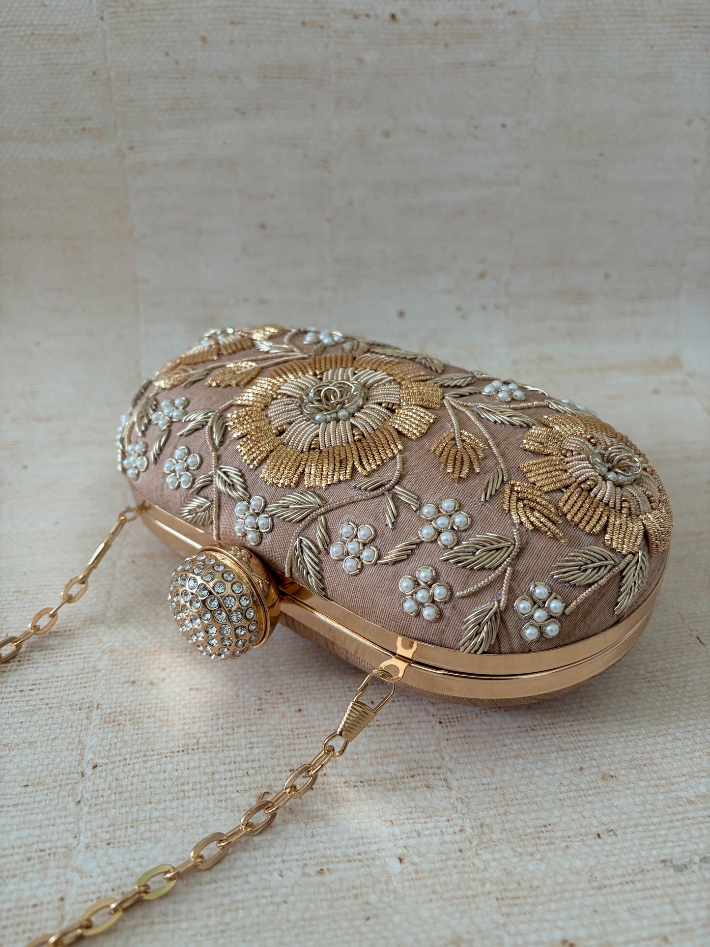 Decorative handbag with floral embroidery and a chain strap on a textured beige background