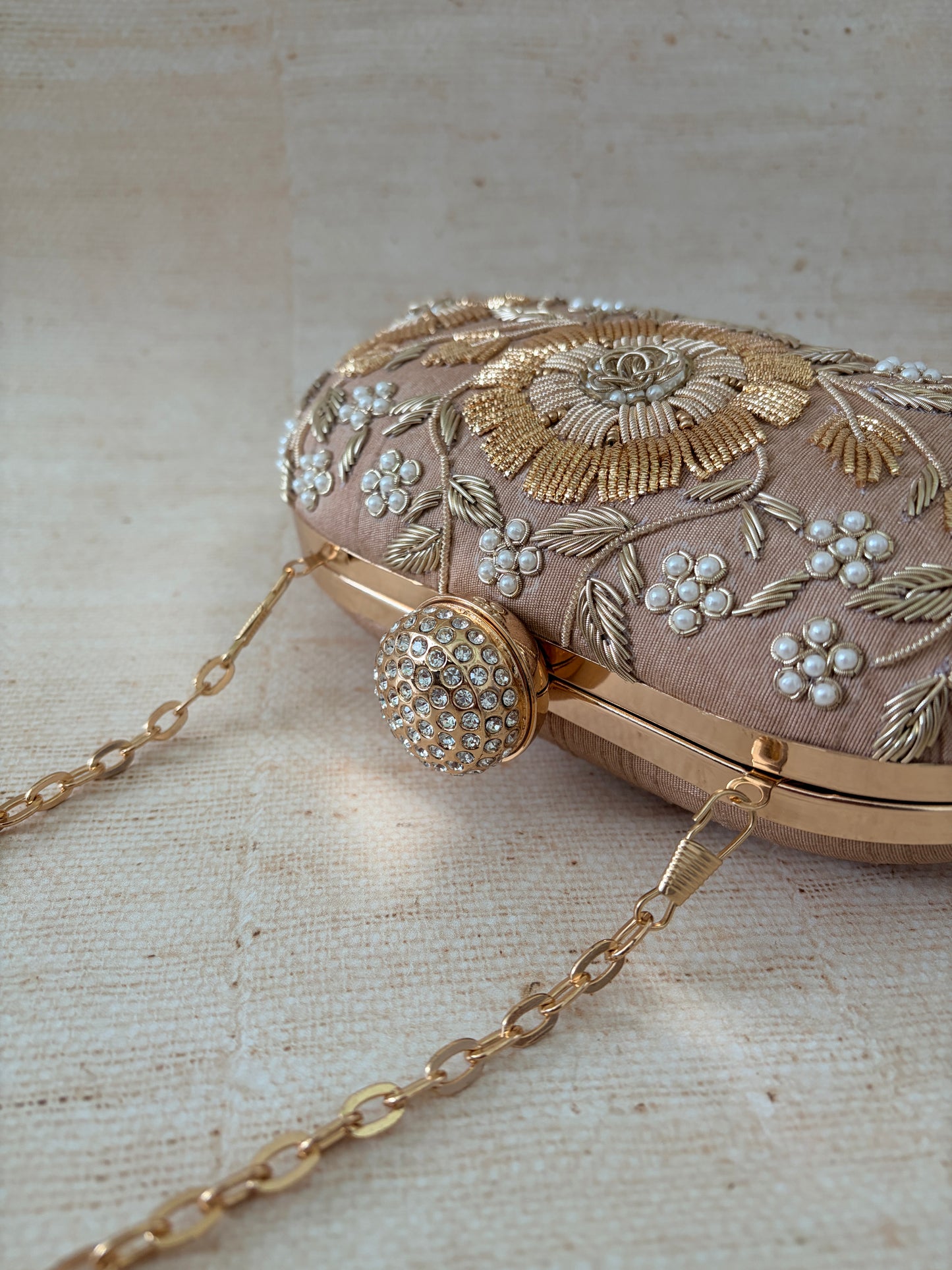 Decorative handbag with floral embroidery and a chain strap on a textured beige background