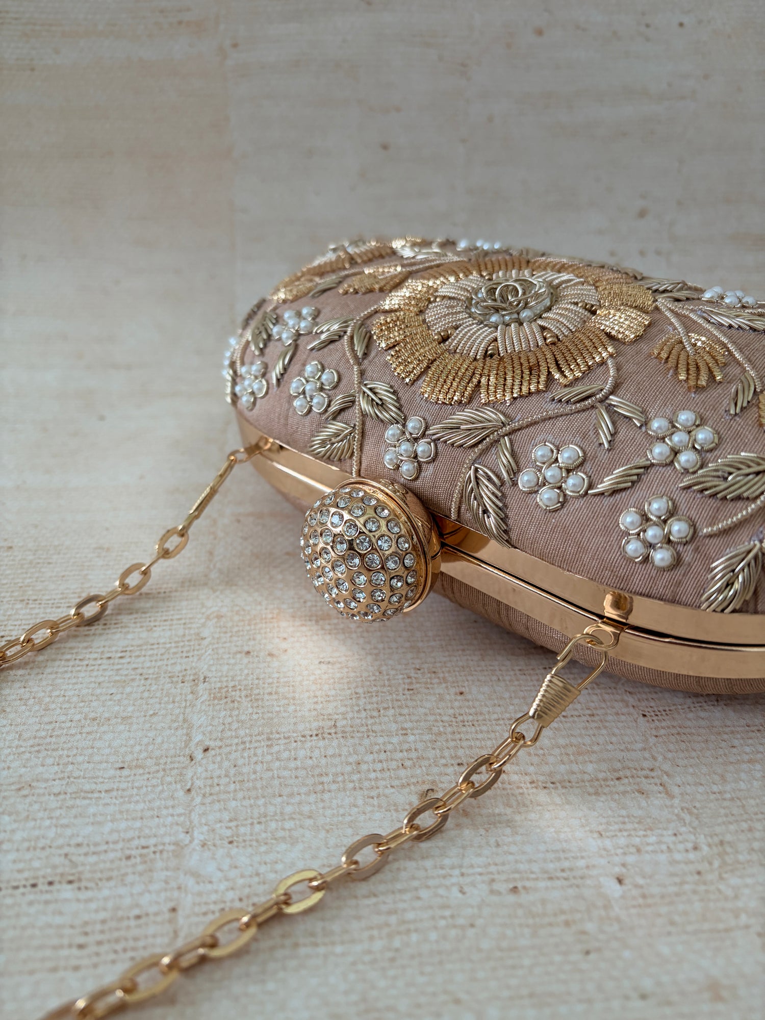 Decorative handbag with floral embroidery and a chain strap on a textured beige background