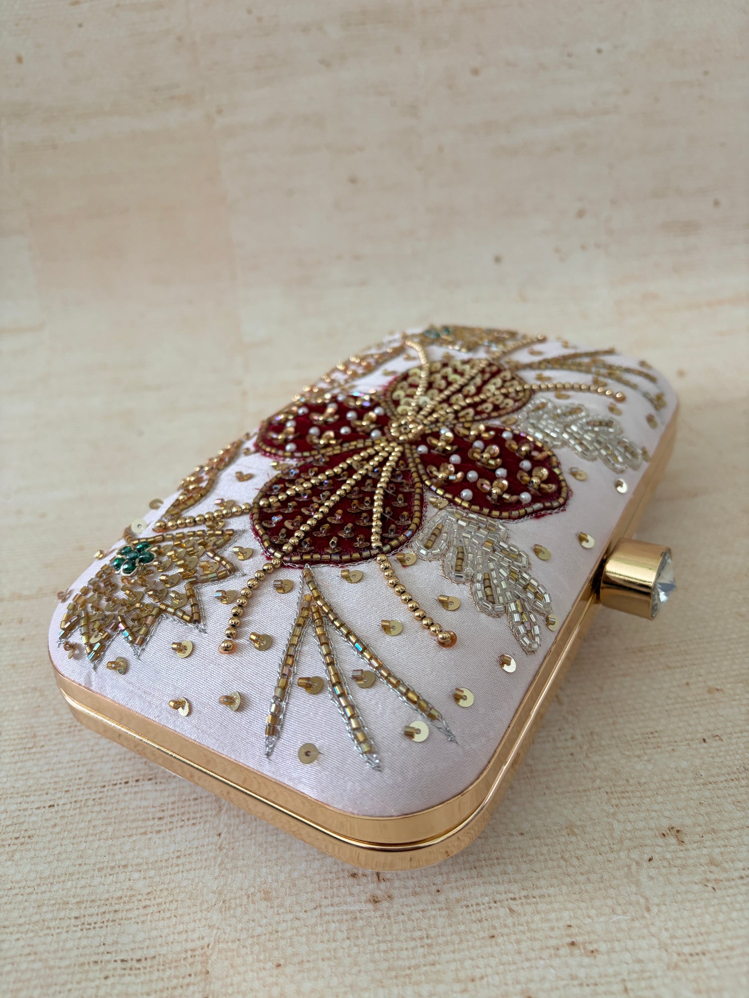 Decorative clutch bag with floral patterns and embellishments on a beige background