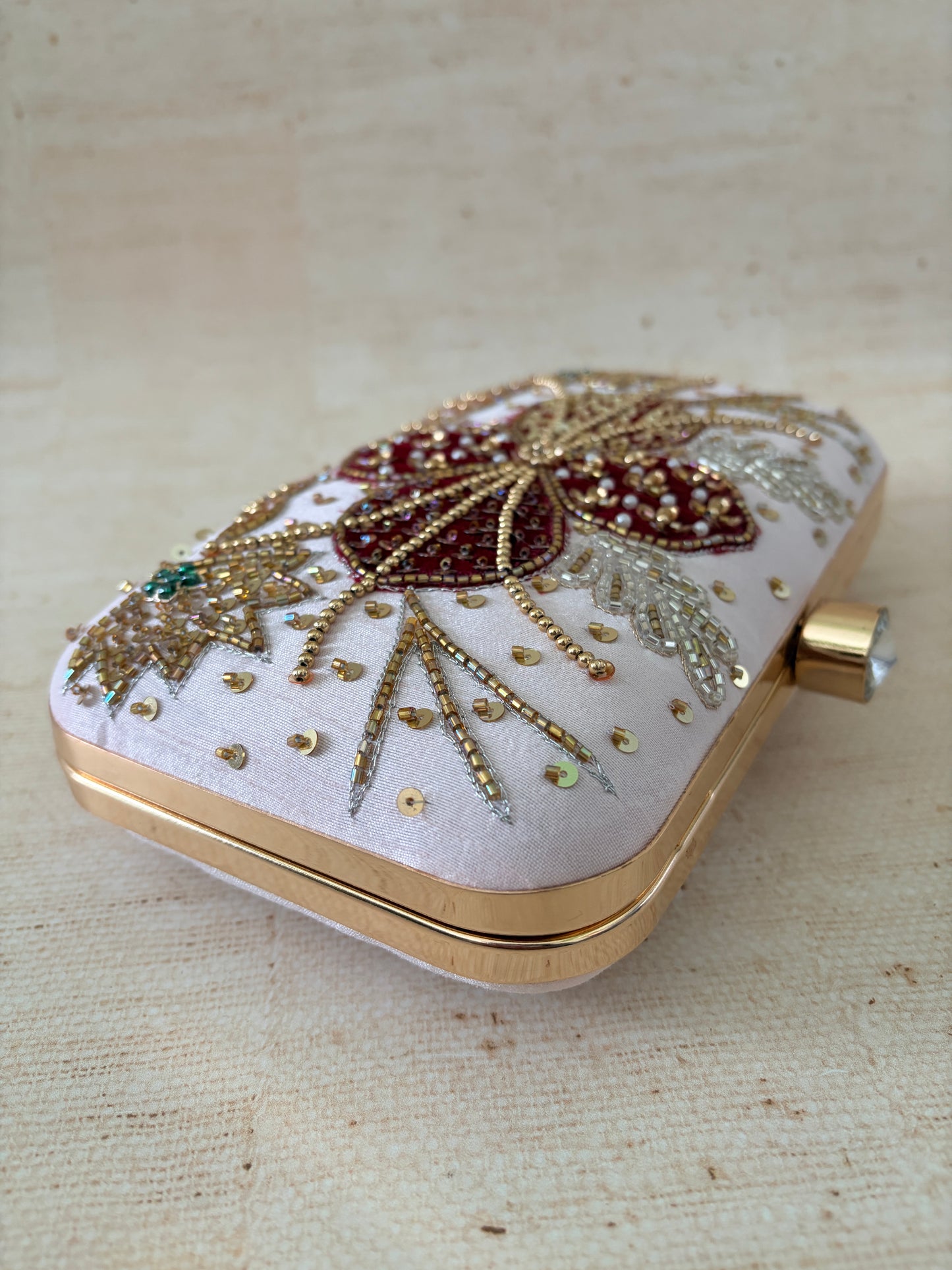 Decorative clutch bag with intricate beadwork on a textured beige background