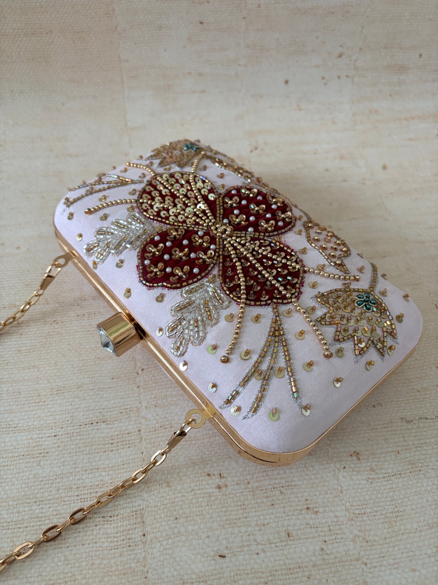 Decorative clutch bag with floral embellishments on a beige fabric background