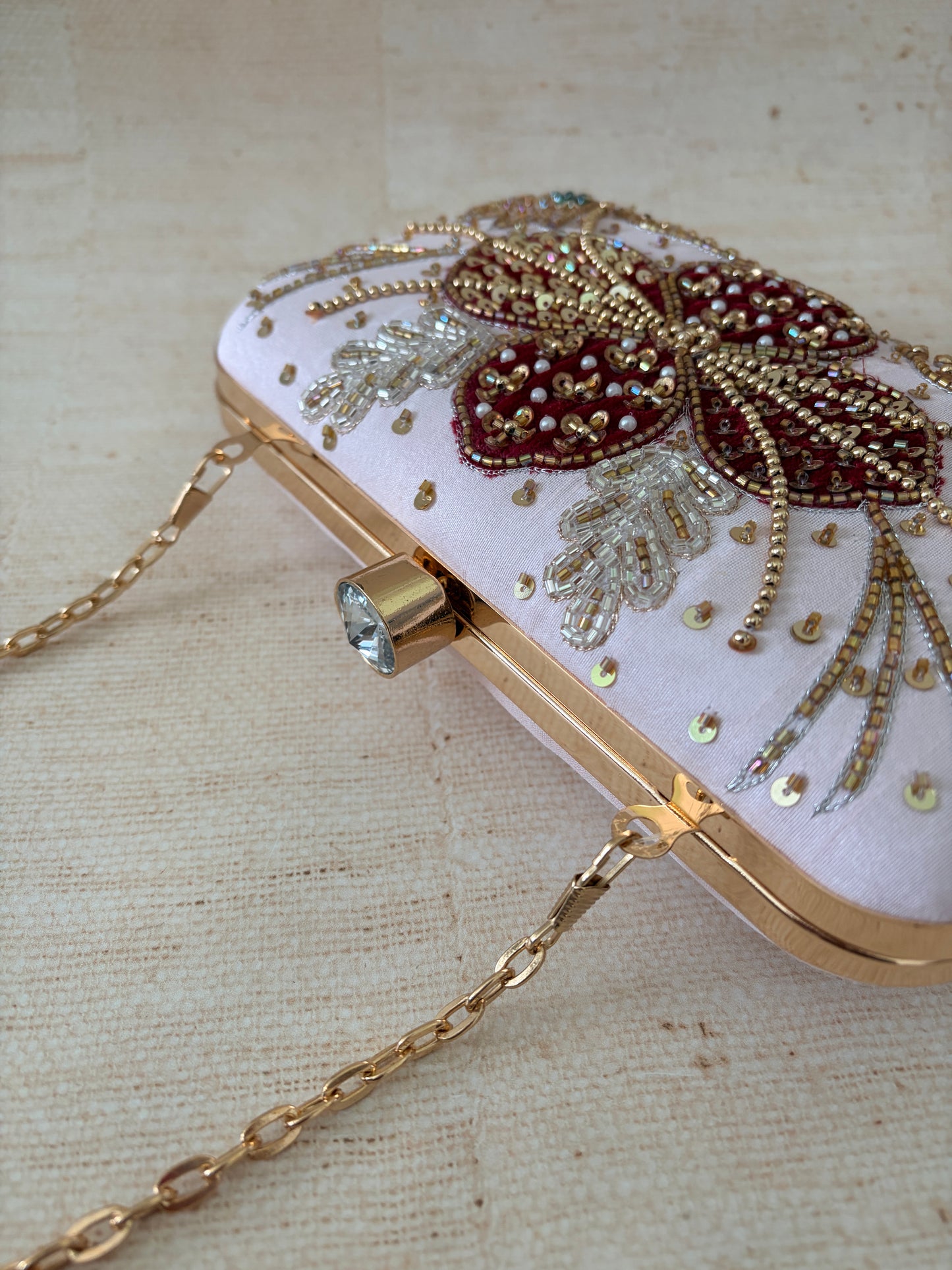 Decorative handbag with floral embellishments and a gold chain on a beige background