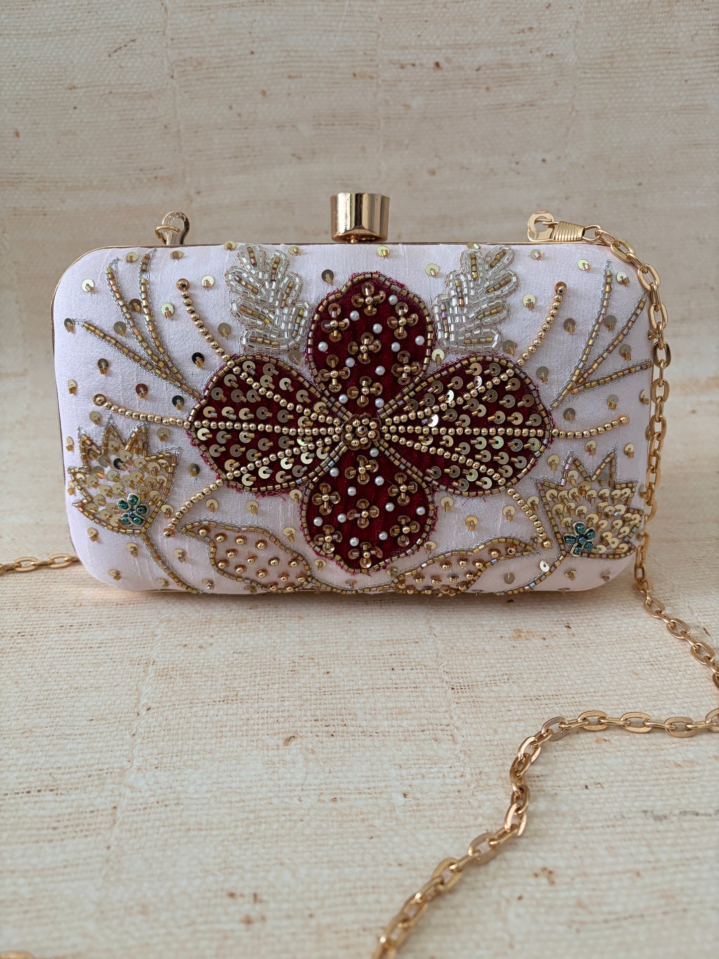 Decorative clutch bag with floral embellishments on a textured beige background