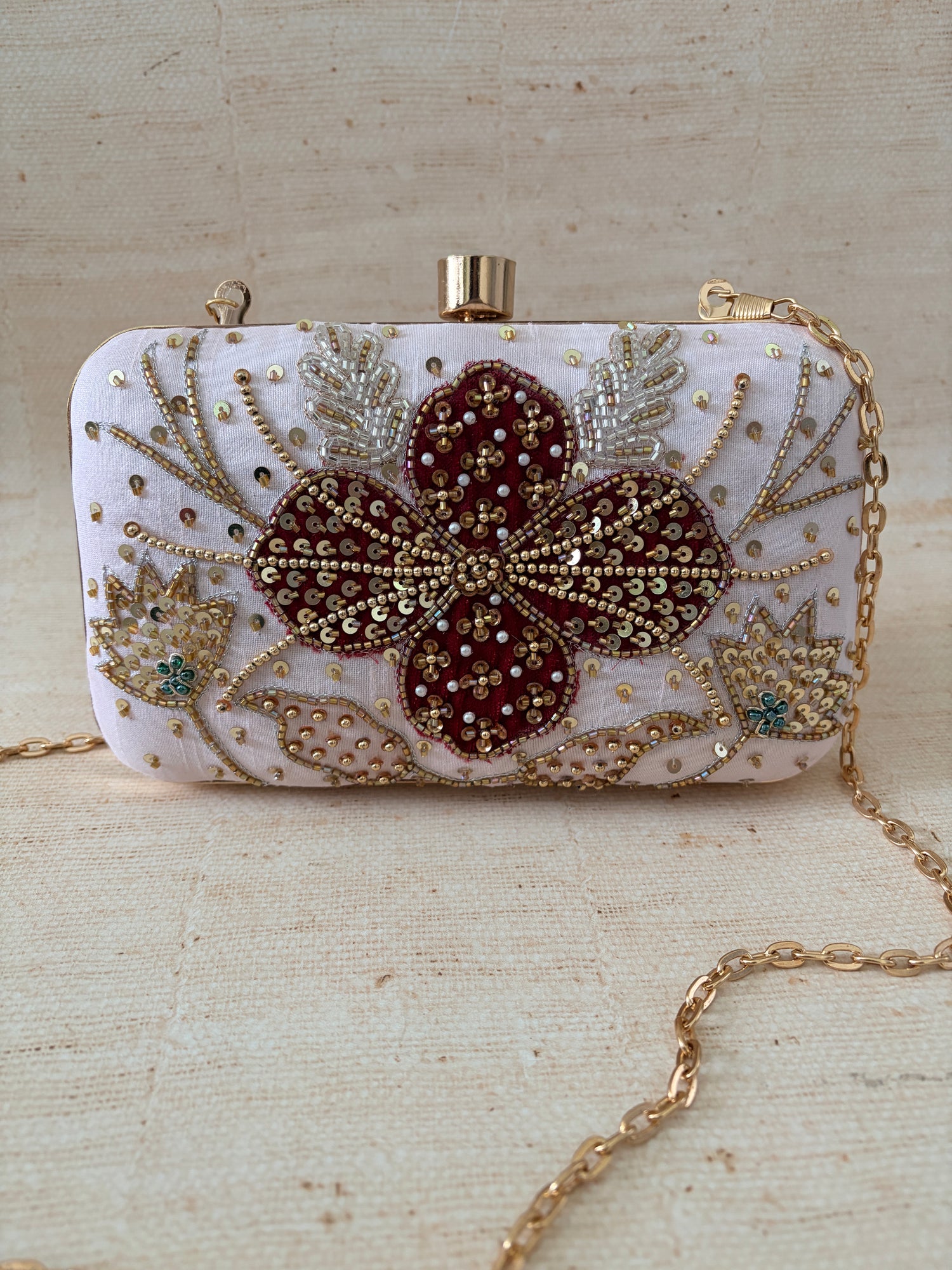 Decorative clutch bag with floral embellishments on a textured beige background