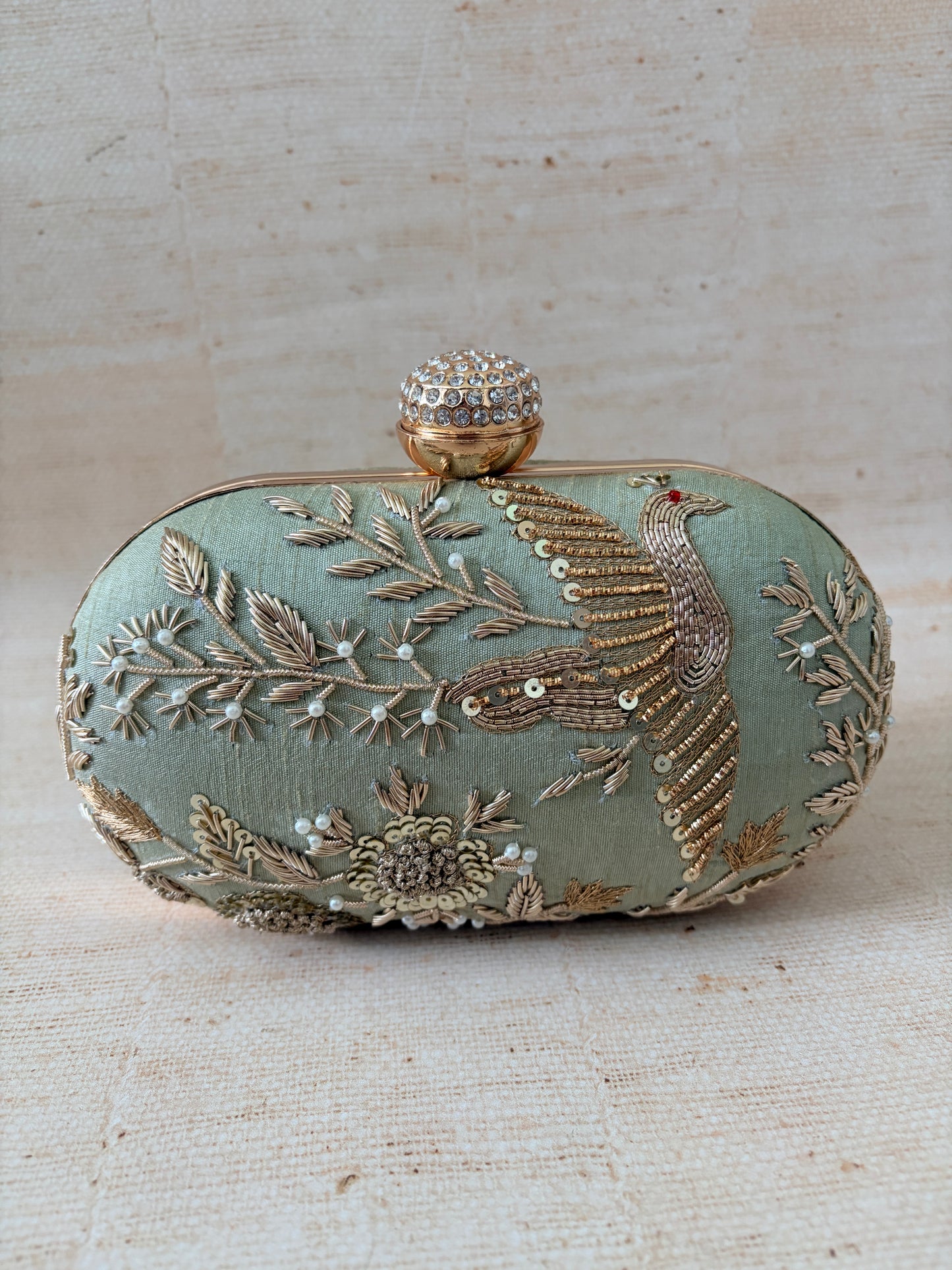 Decorative clutch bag with floral embroidery on a textured beige background