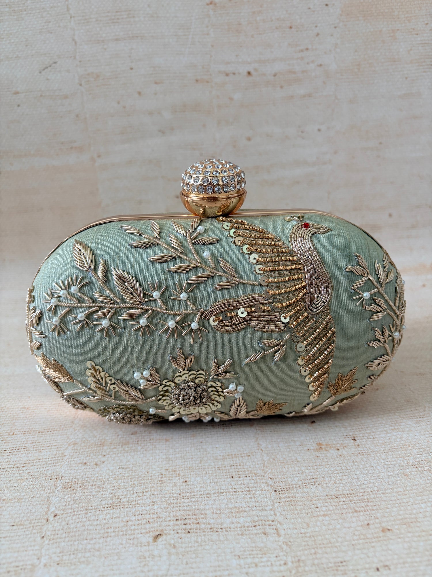 Decorative clutch bag with floral embroidery on a textured beige background