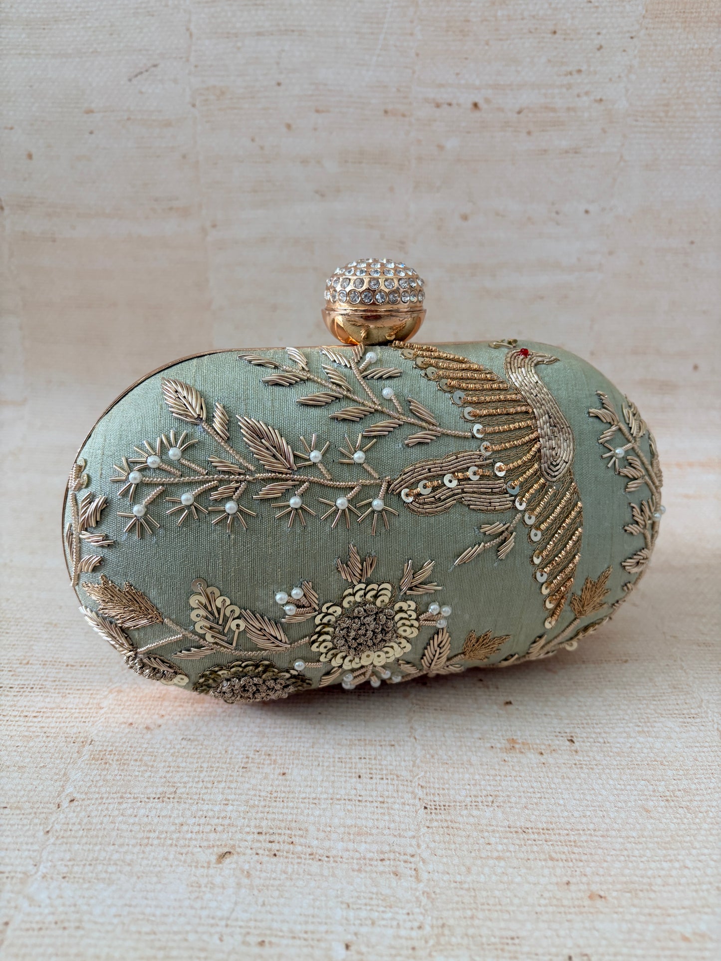 Decorative clutch bag with intricate embroidery on a textured beige background