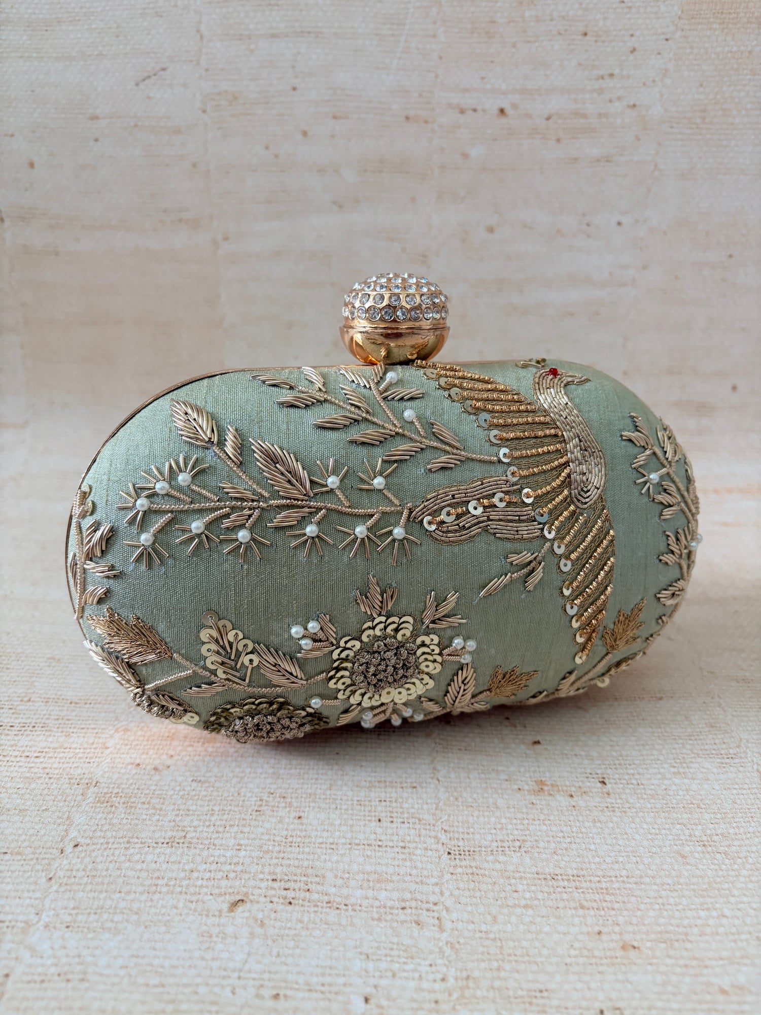 Decorative clutch bag with intricate embroidery on a textured beige background