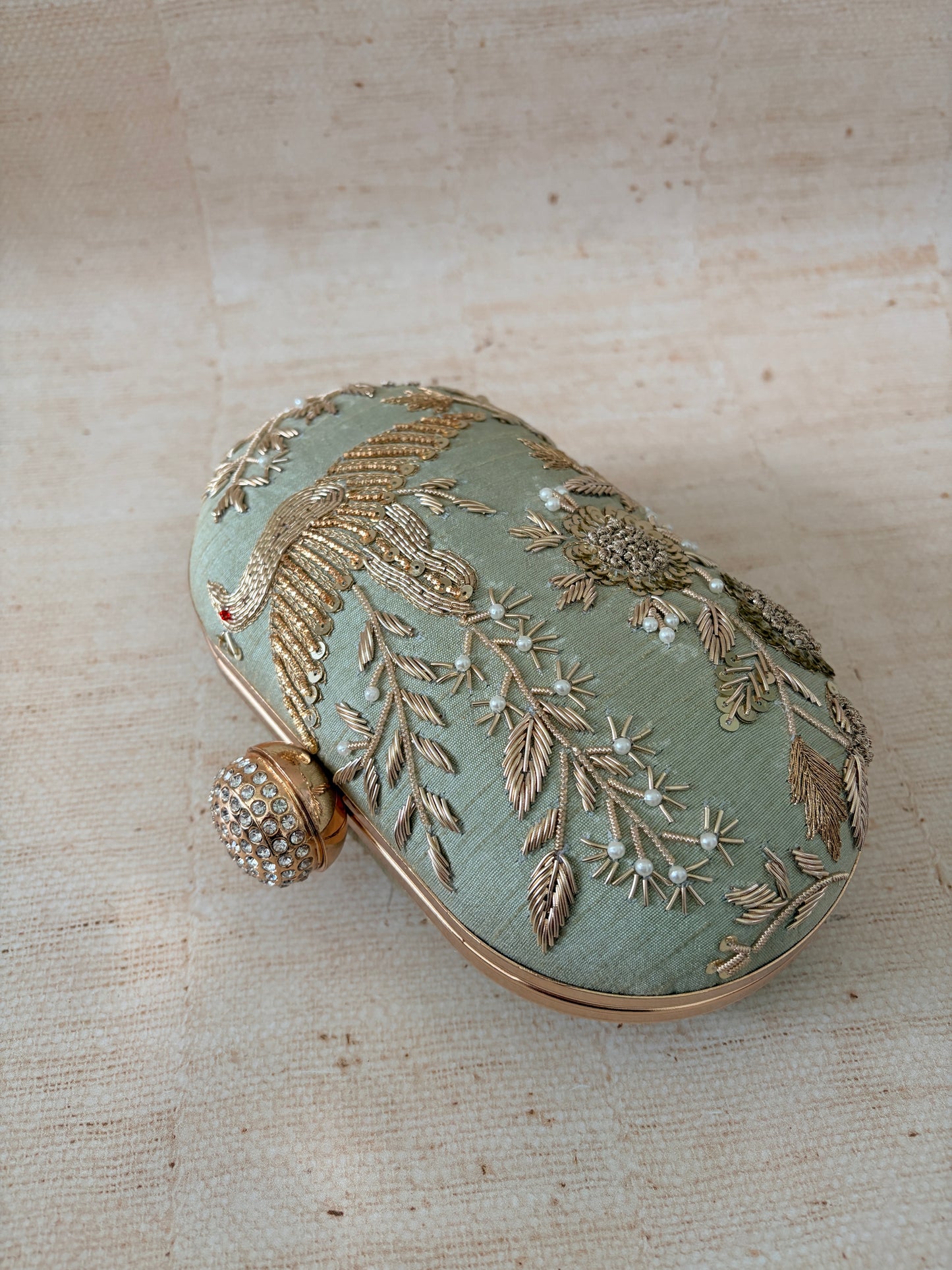 Decorative round clutch with floral embroidery on a textured beige background