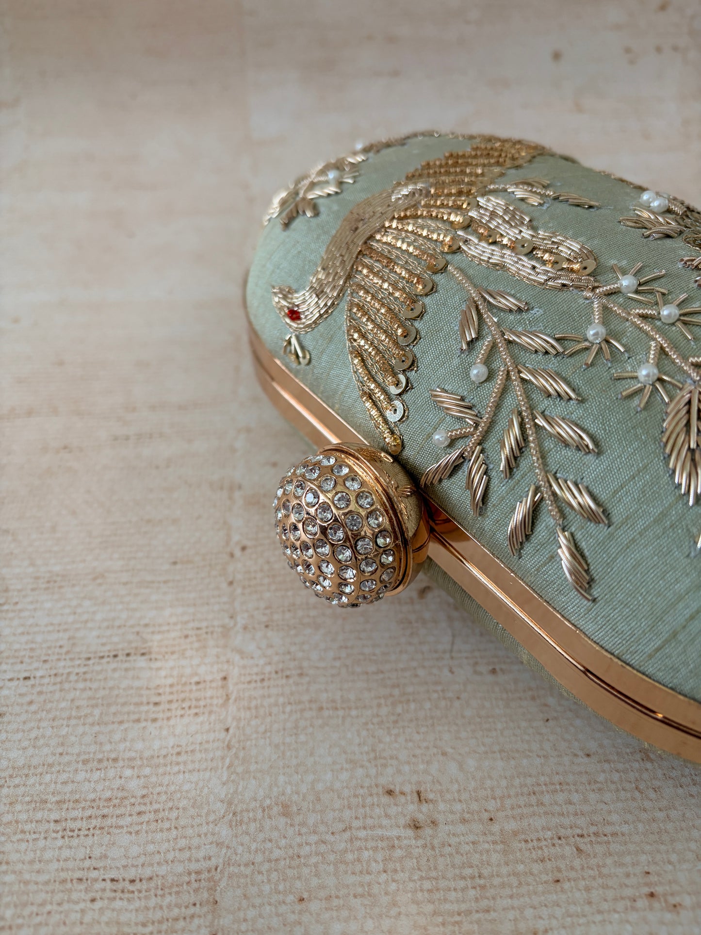 Decorative clutch with intricate gold embroidery on a textured beige background