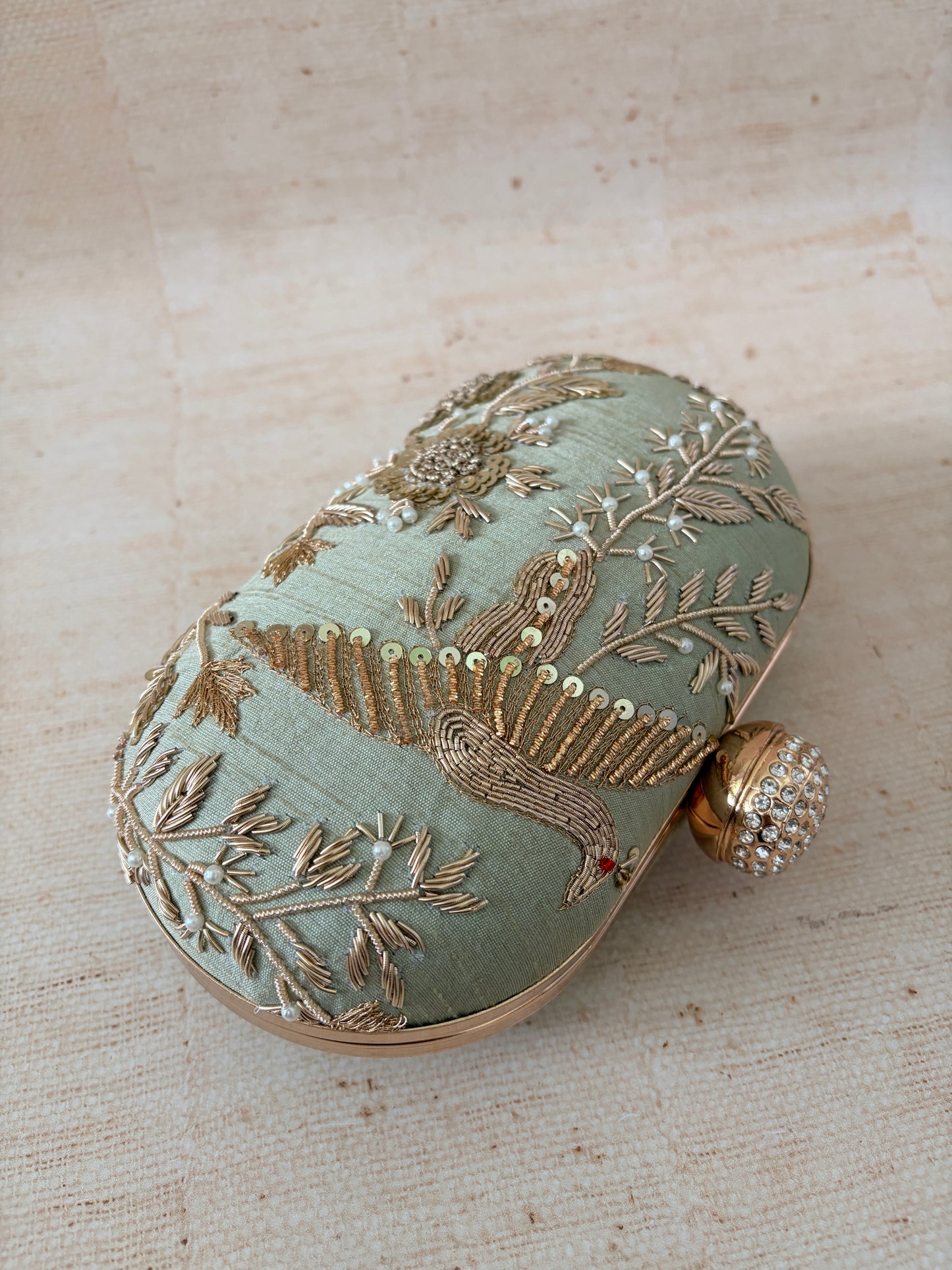 Decorative clutch with intricate gold embroidery on a textured beige background