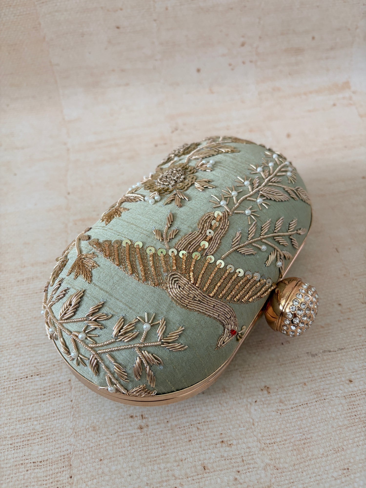 Decorative clutch with intricate gold embroidery on a textured beige background