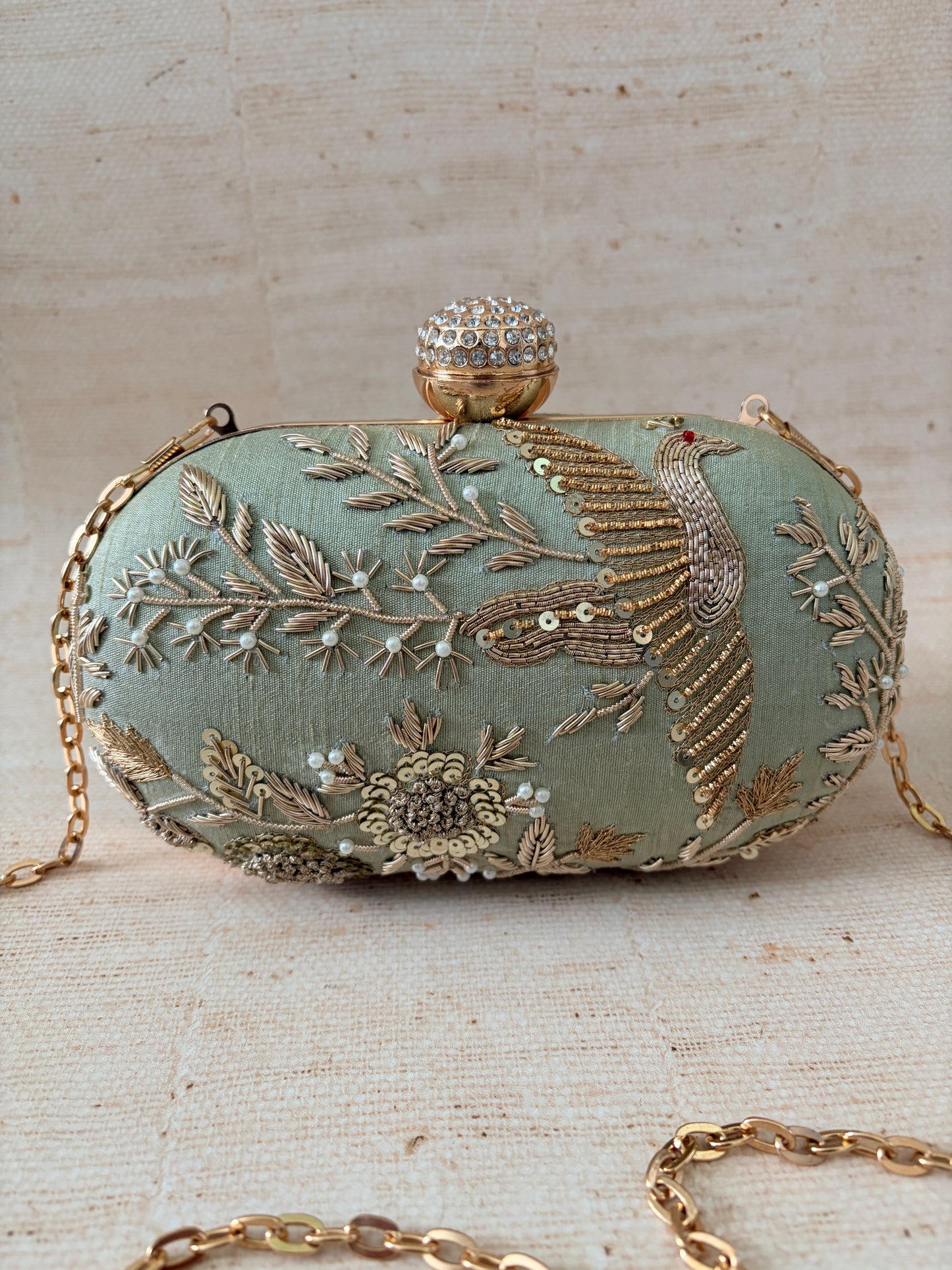 Decorative clutch bag with intricate gold embroidery on a textured beige background