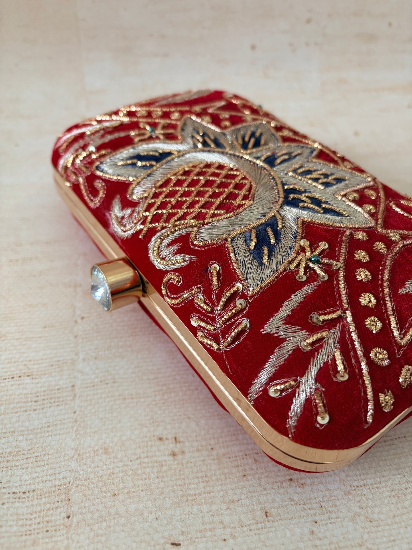 Red clutch with gold and silver embroidery on a beige fabric background