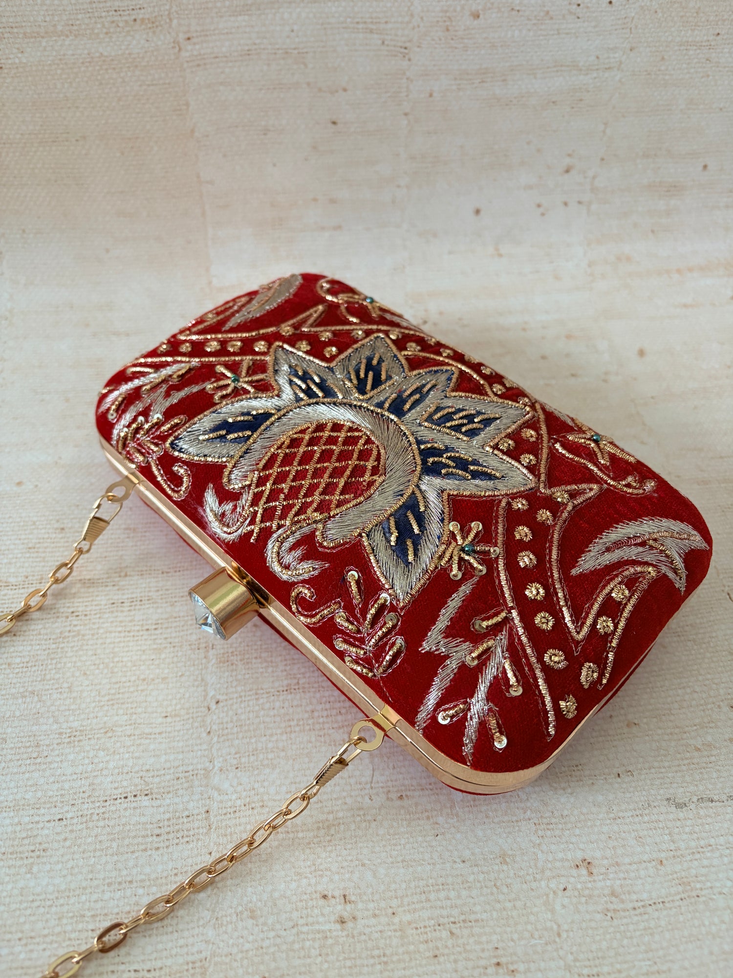 Red clutch bag with floral embroidery and gold chain on a beige background