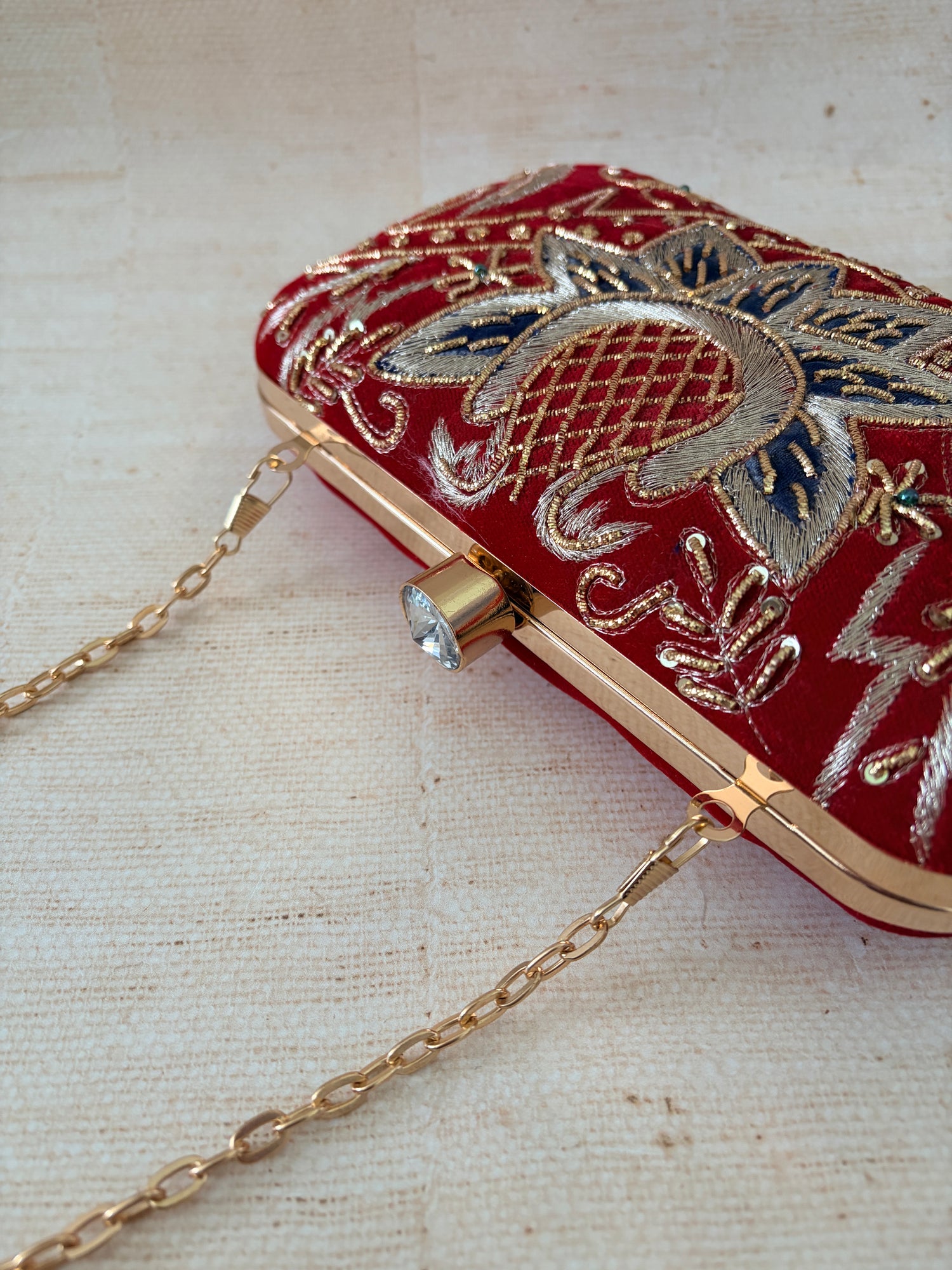 Red clutch with gold chain strap and intricate gold embroidery on a light beige background