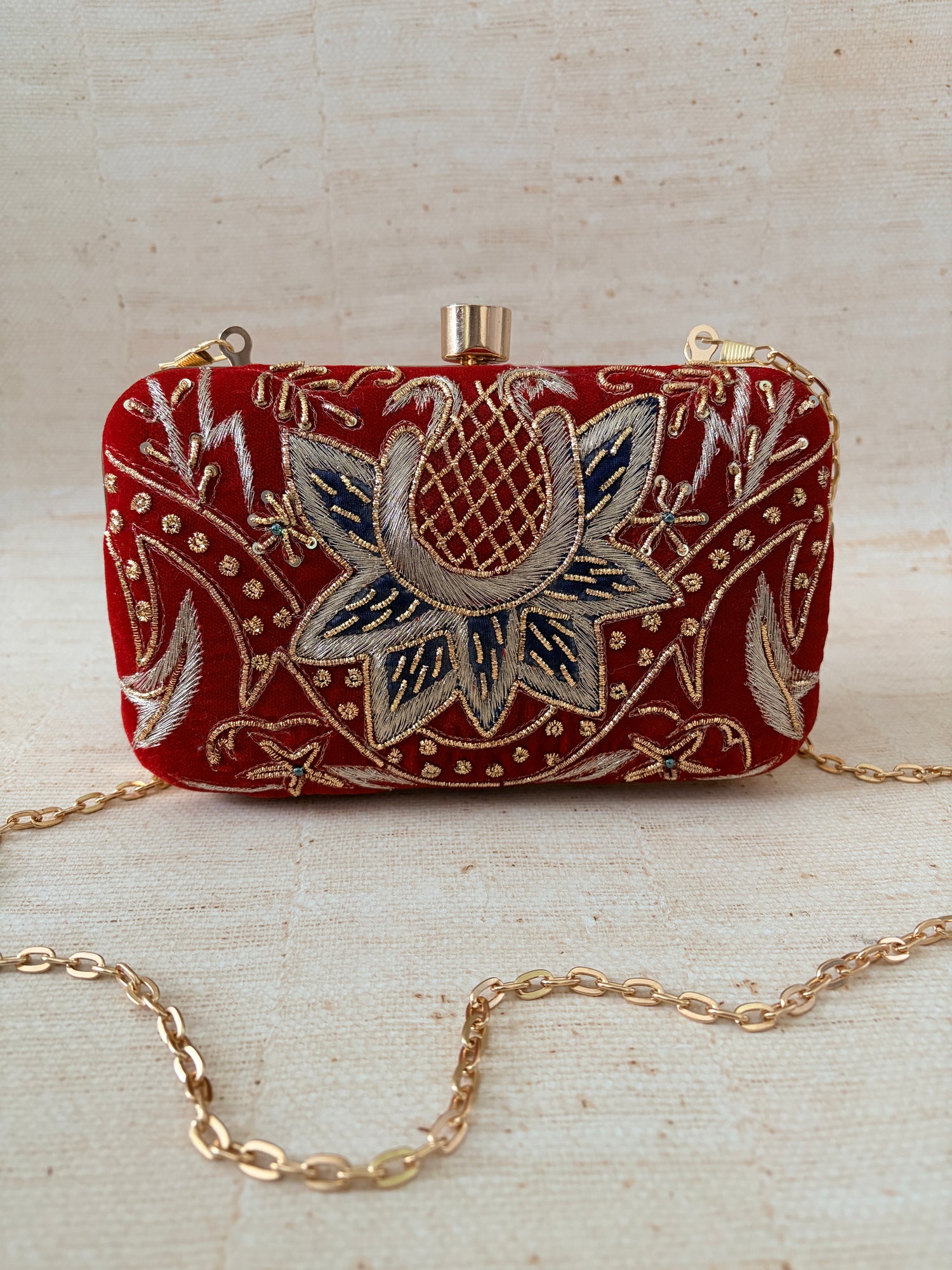 Decorative red pouch with floral embroidery and gold chain on a beige background