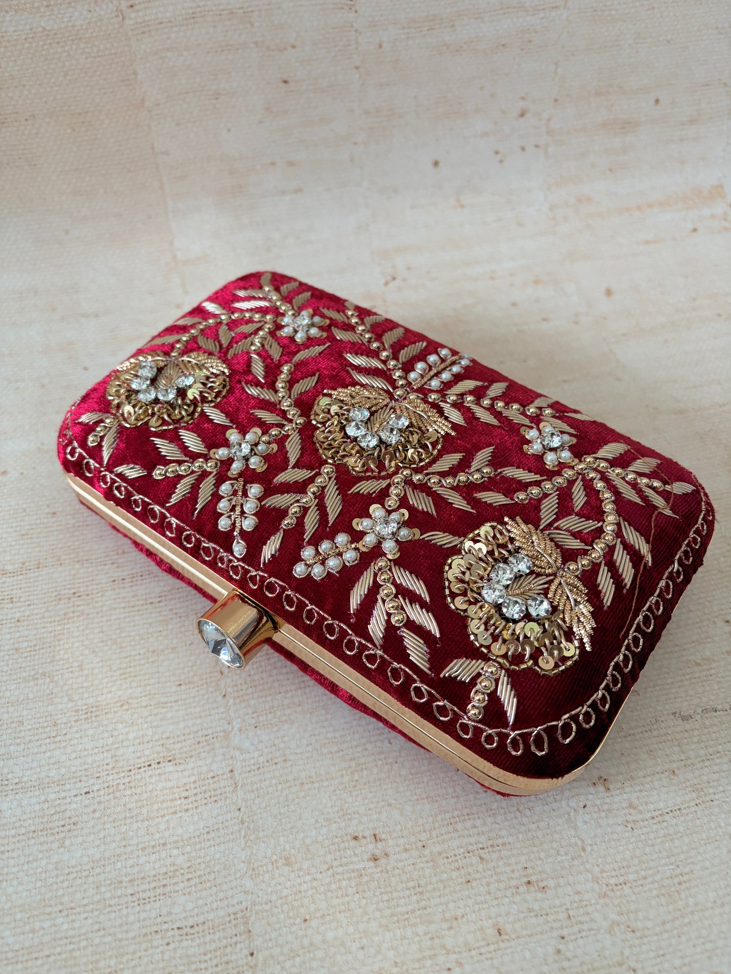 Decorative red clutch with gold embroidery on a beige background