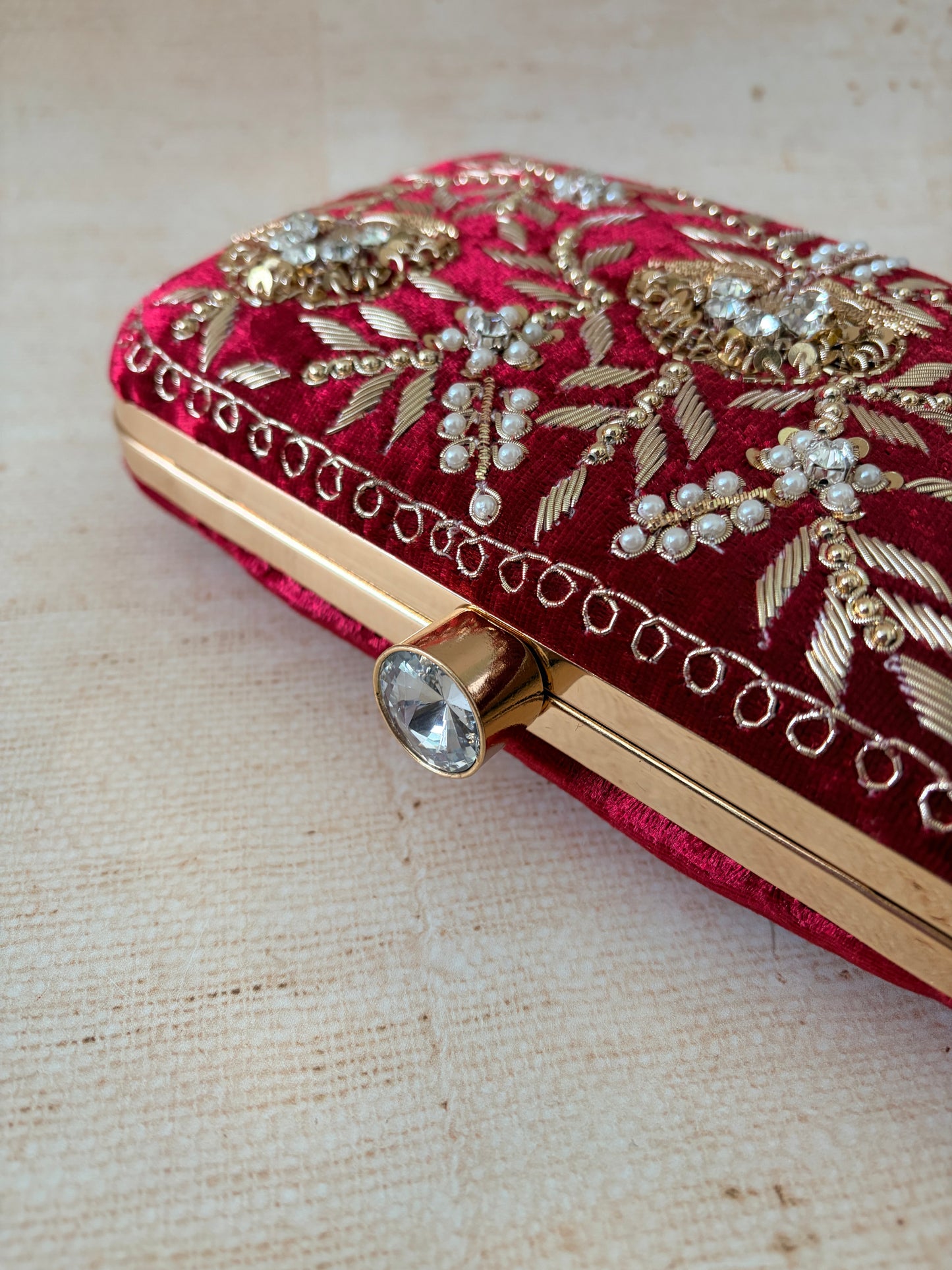 Red clutch with gold embroidery and embellishments on a beige fabric background