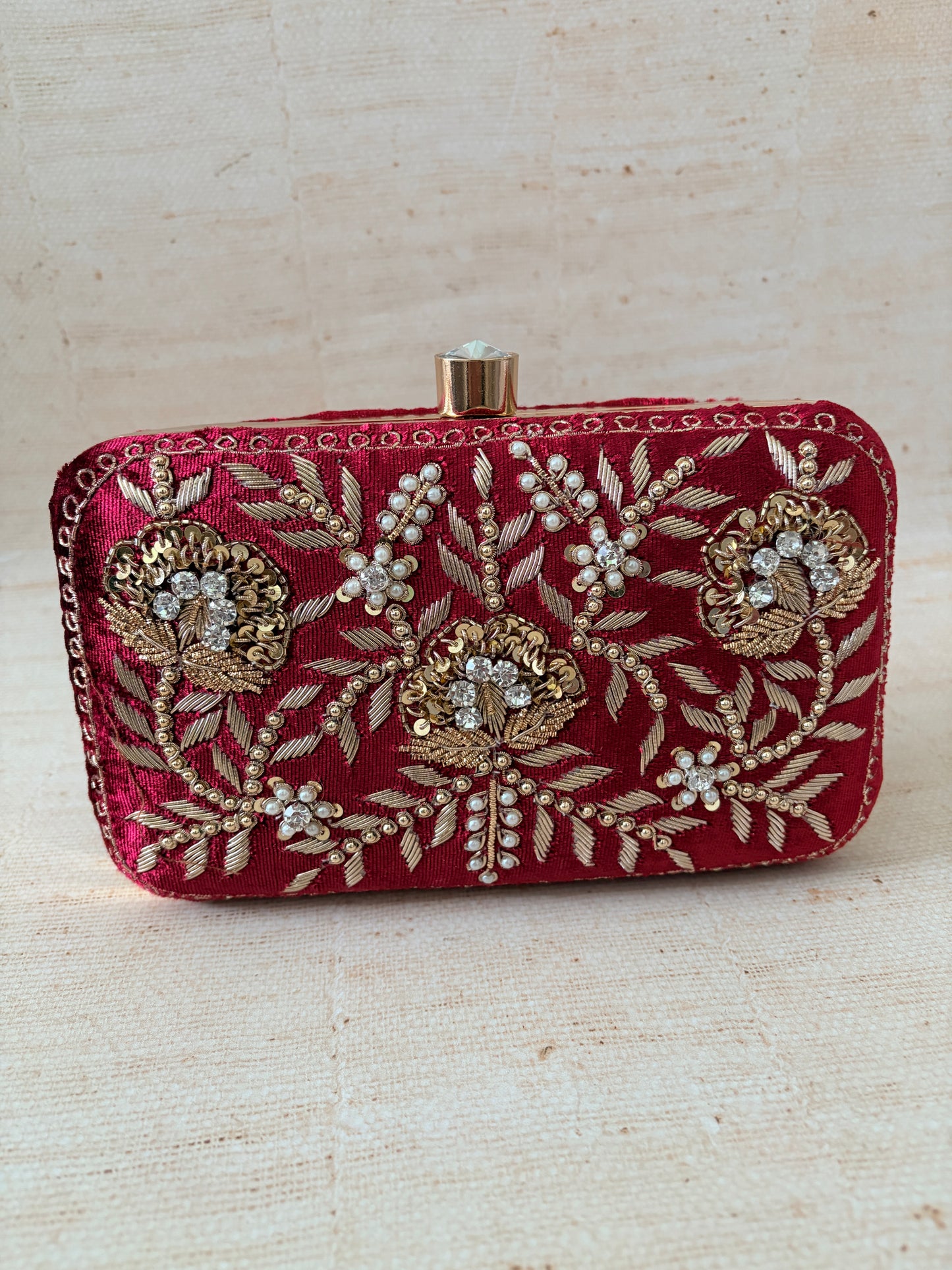 Decorative red clutch with gold embroidery on a beige background