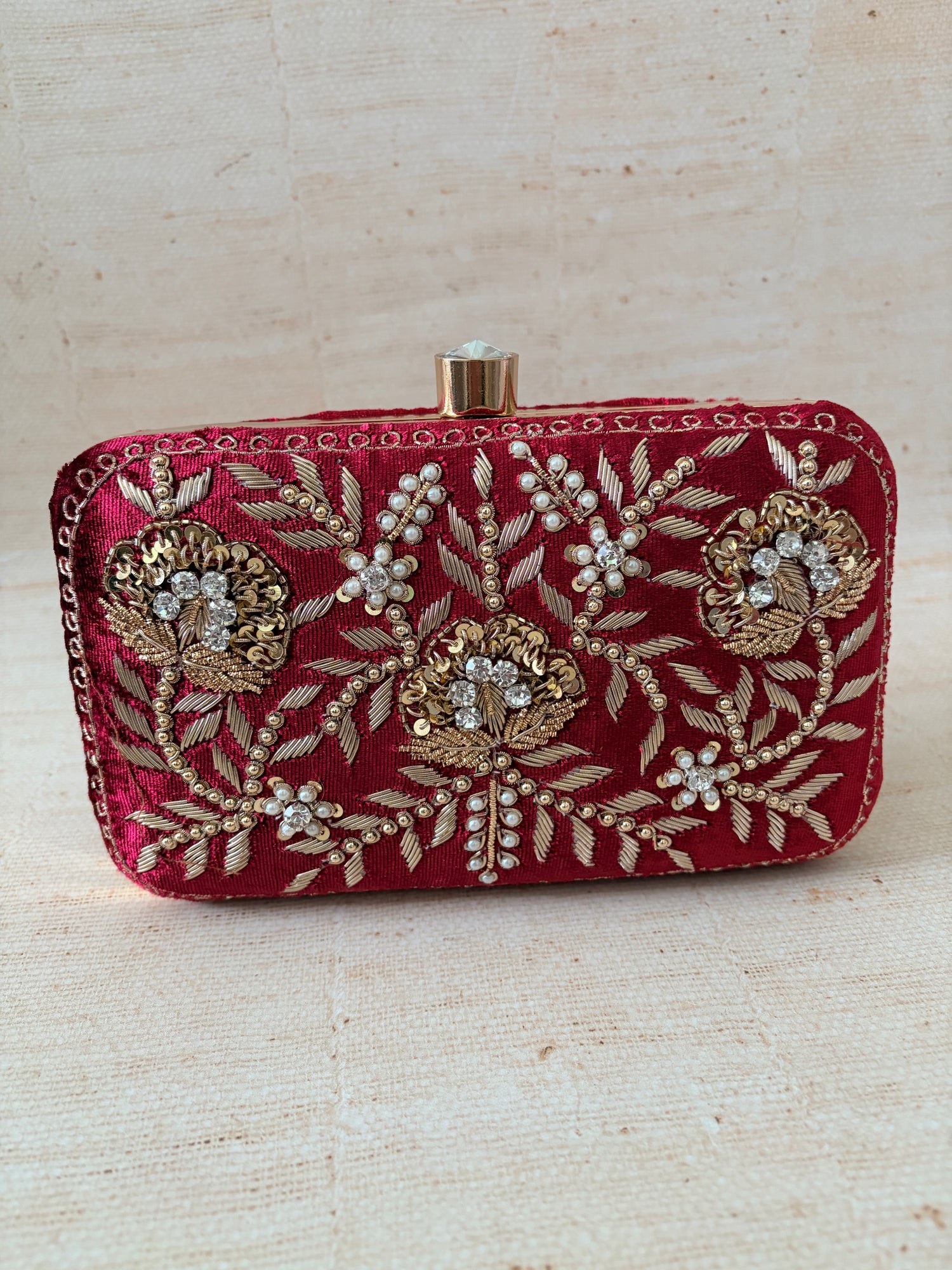 Decorative red clutch with gold embroidery on a beige background