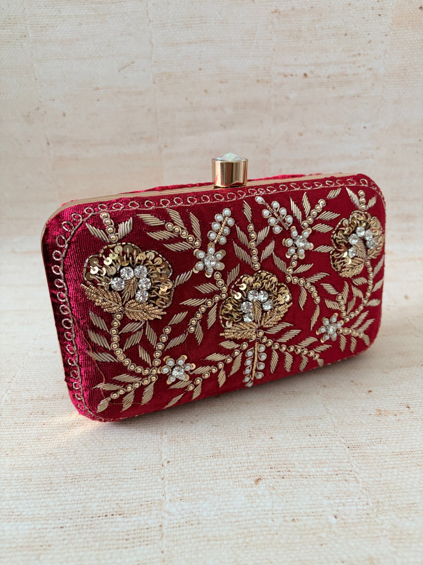 Red embroidered clutch with gold patterns on a beige background