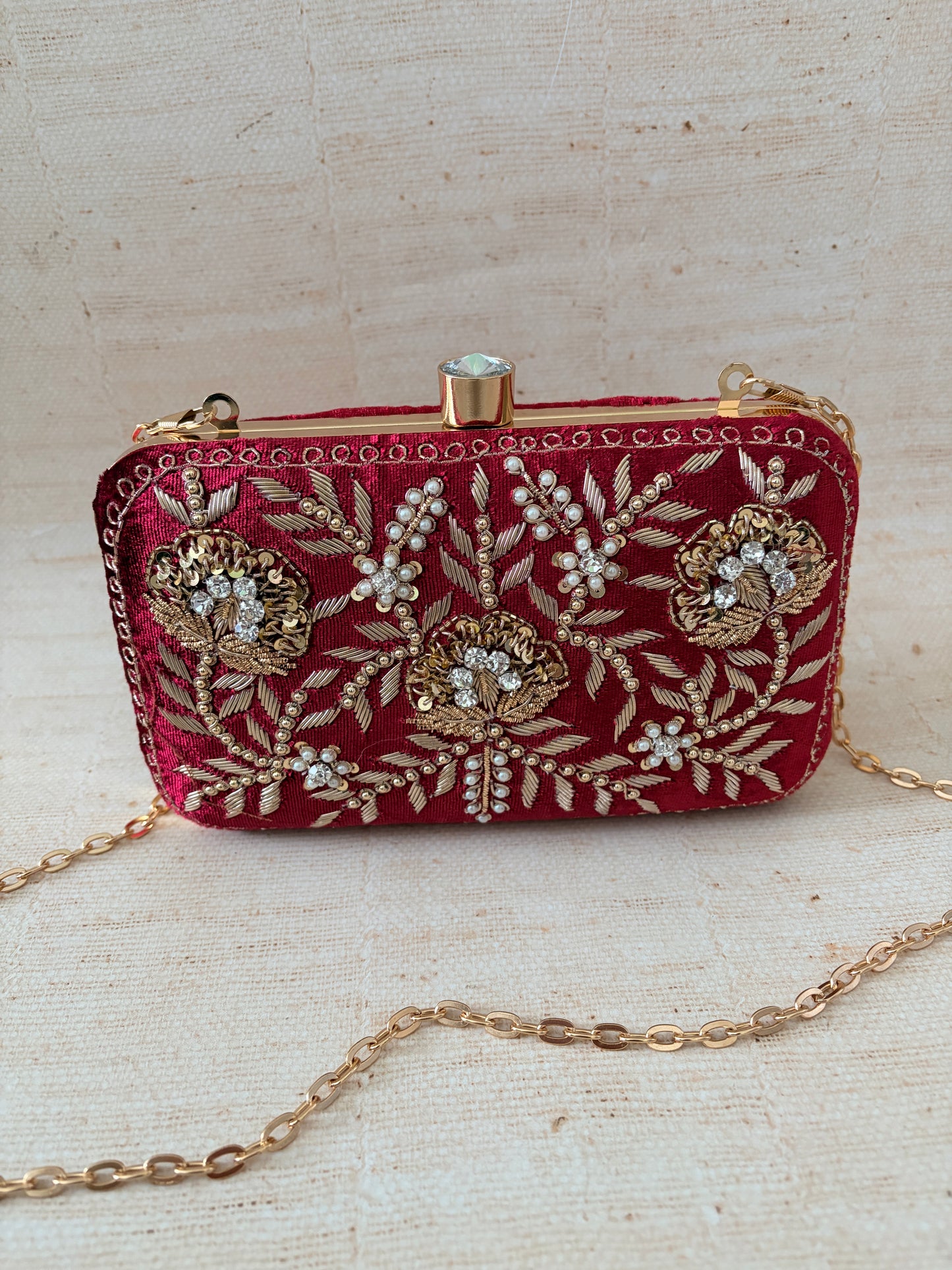 Red embroidered clutch bag with gold chain on a textured beige background