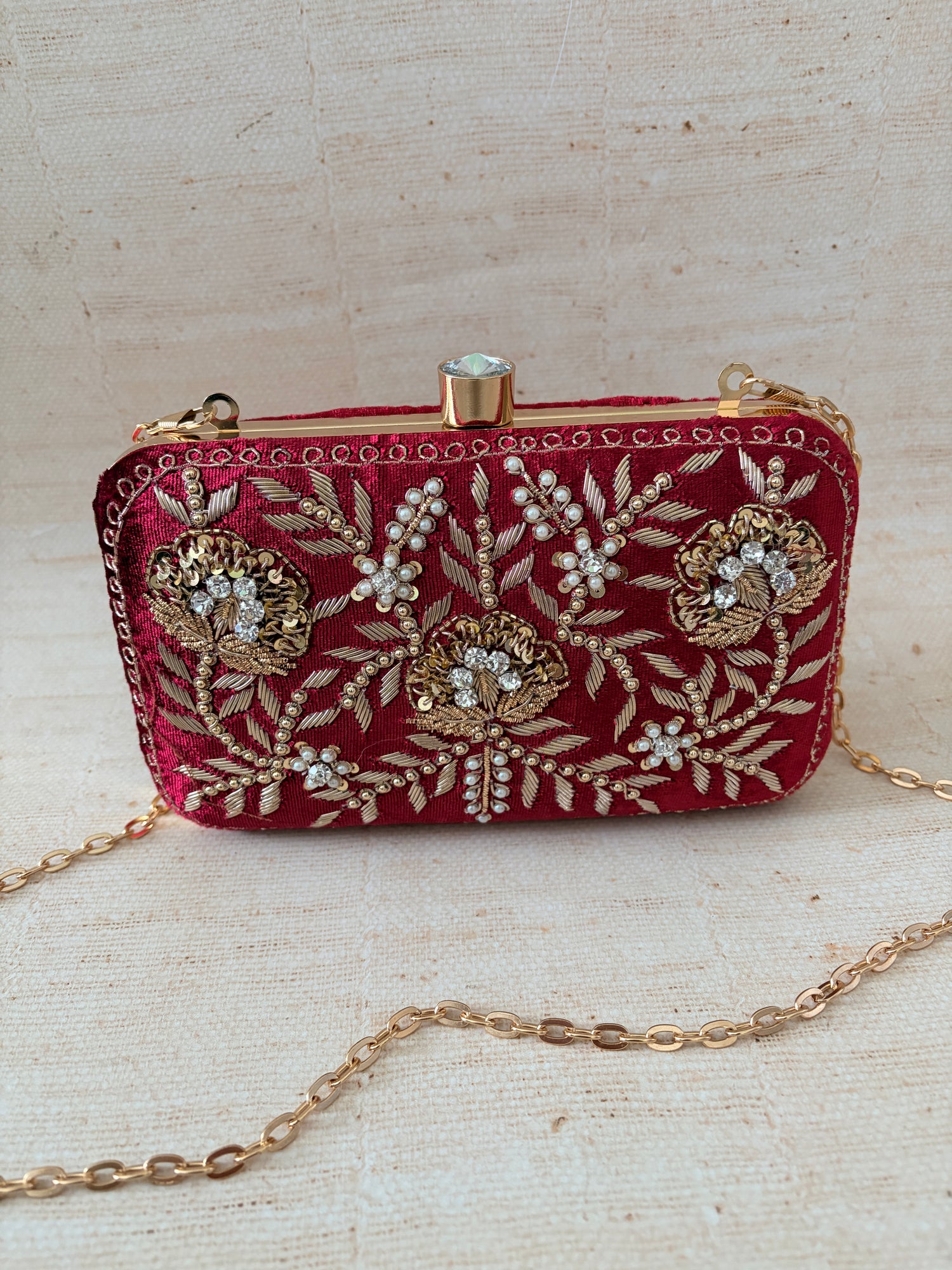 Red embroidered clutch bag with gold chain on a textured beige background