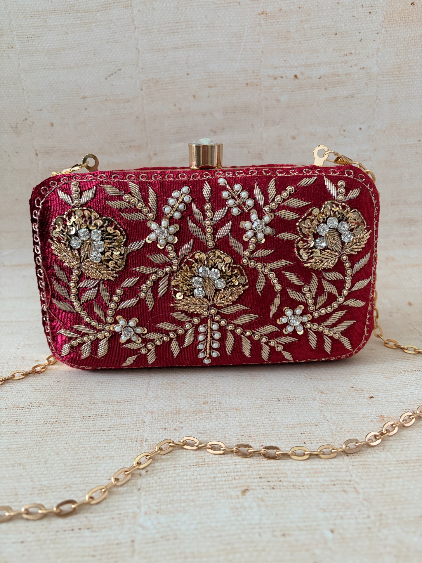 Decorative red clutch with gold embroidery on a textured beige background