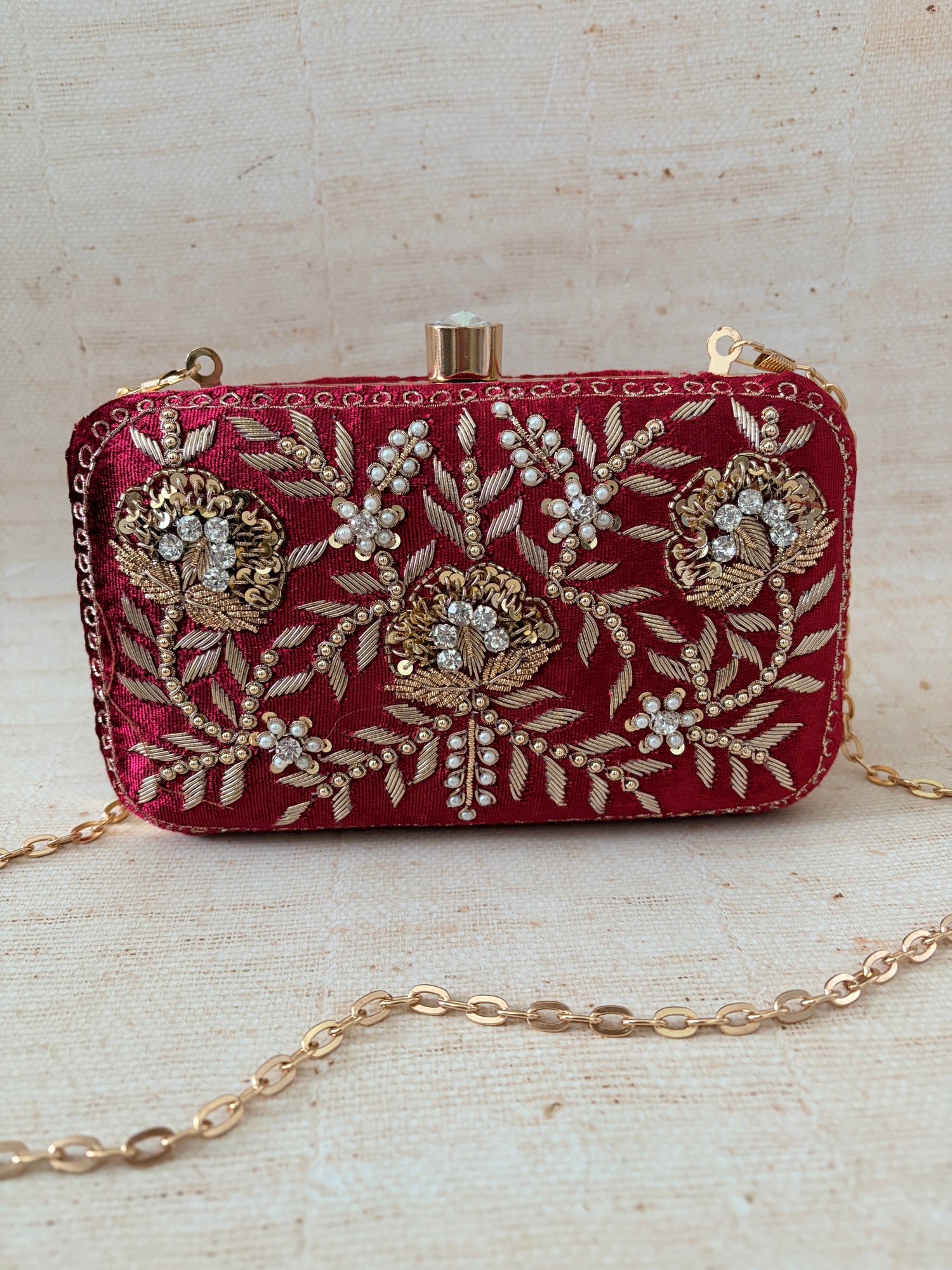 Decorative red clutch with gold embroidery on a textured beige background