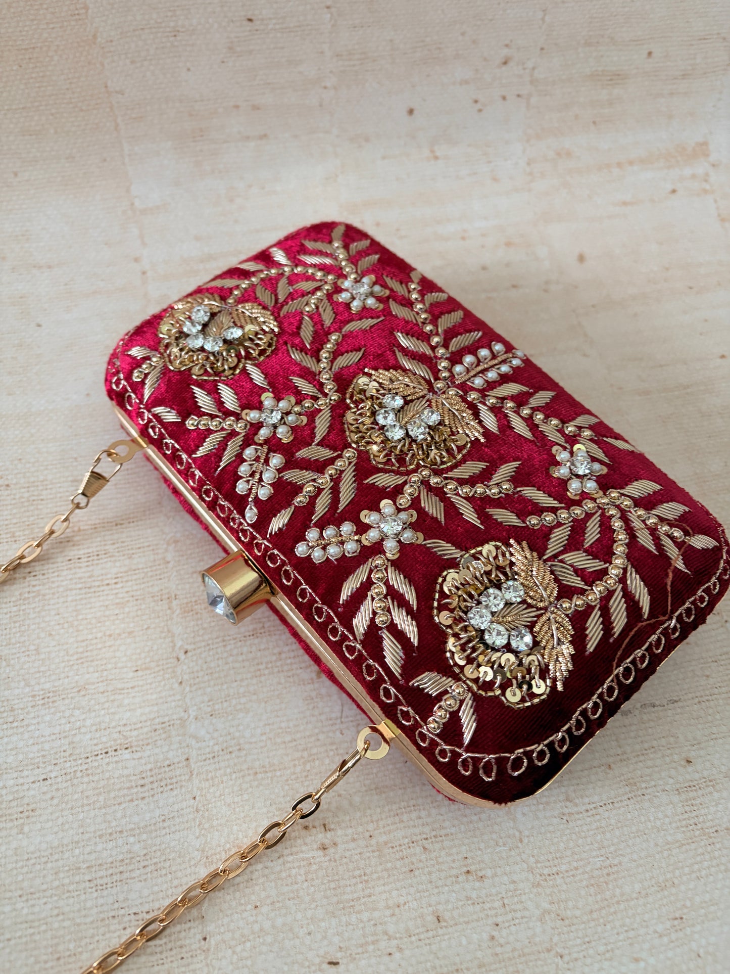 Decorative red clutch bag with gold embroidery on a beige background