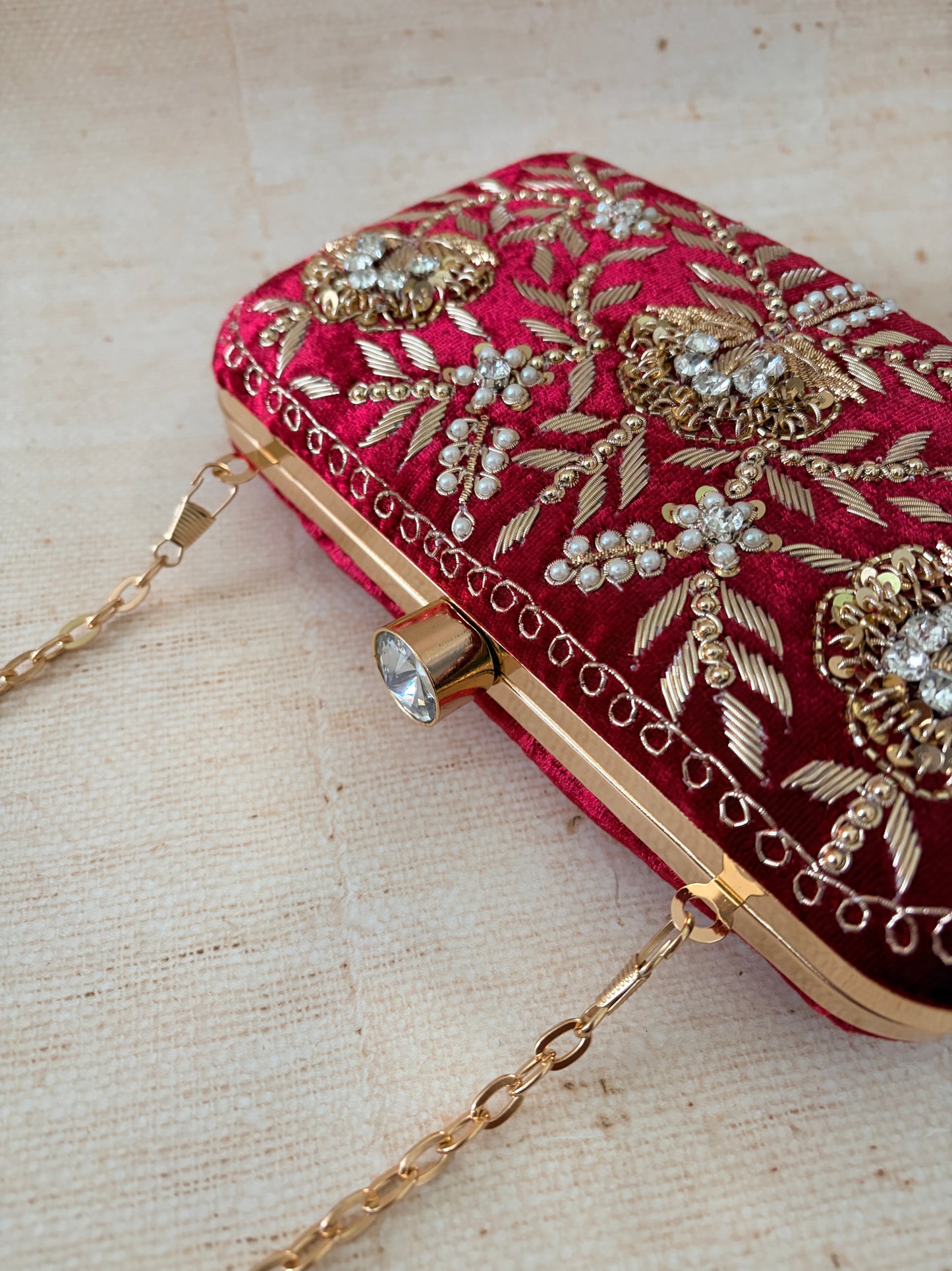 Red clutch bag with gold embroidery and embellishments on a beige fabric background