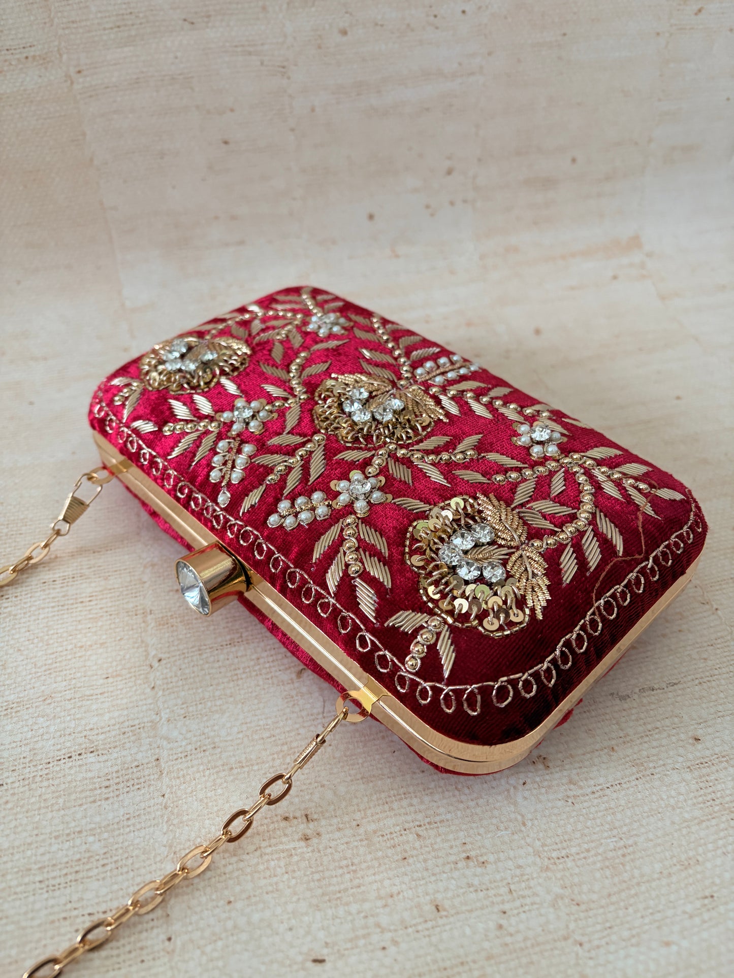 Red clutch bag with gold embroidery and embellishments on a beige background