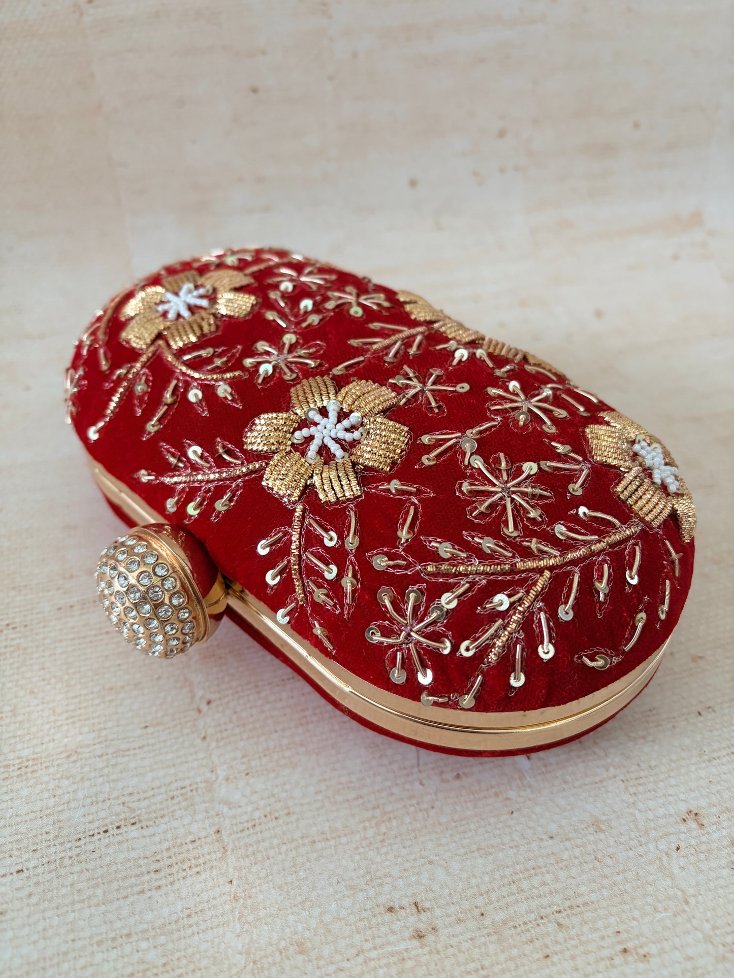Red clutch with gold and silver embroidery on a textured beige background