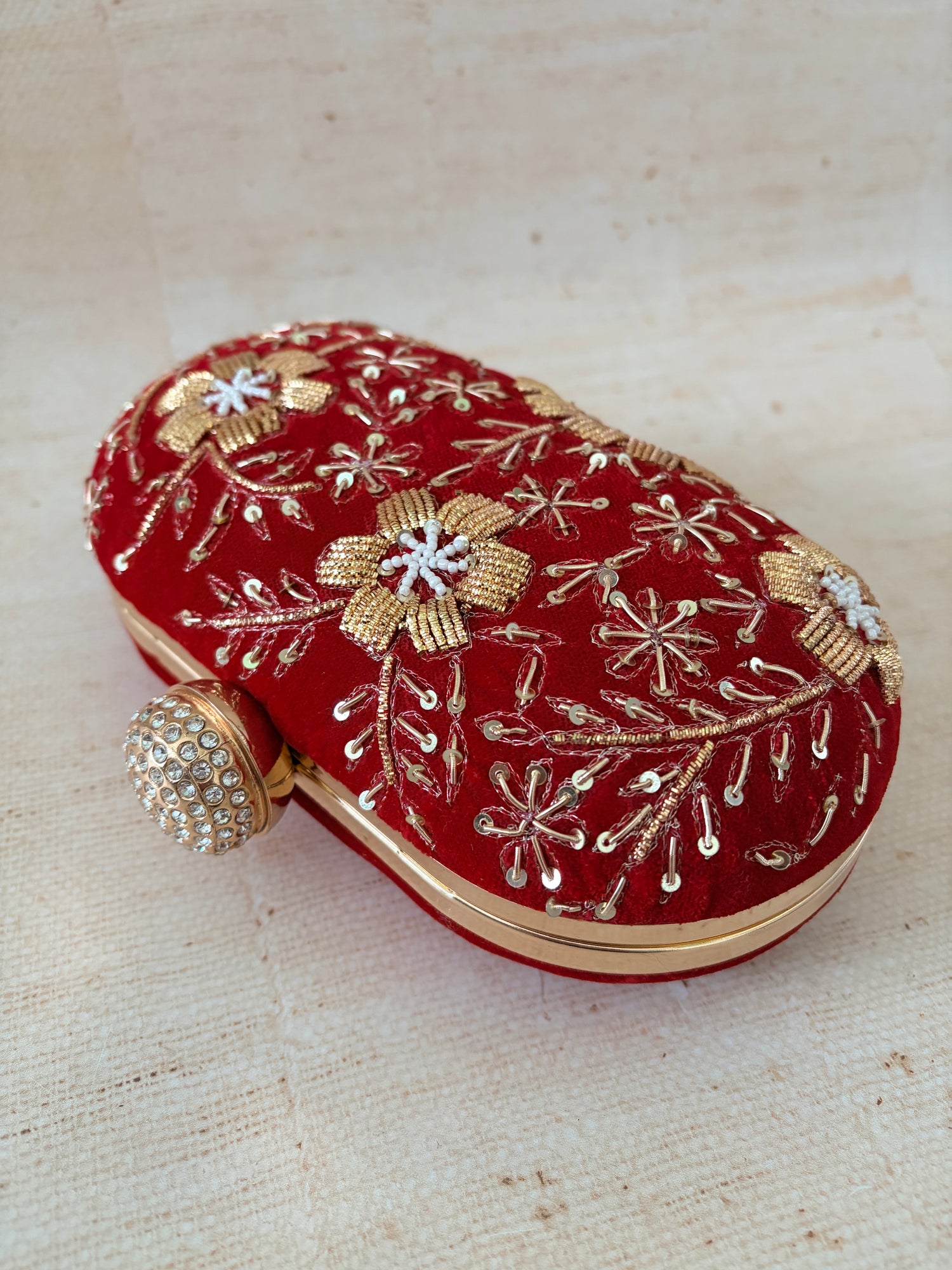 Red clutch with gold and silver embroidery on a textured beige background
