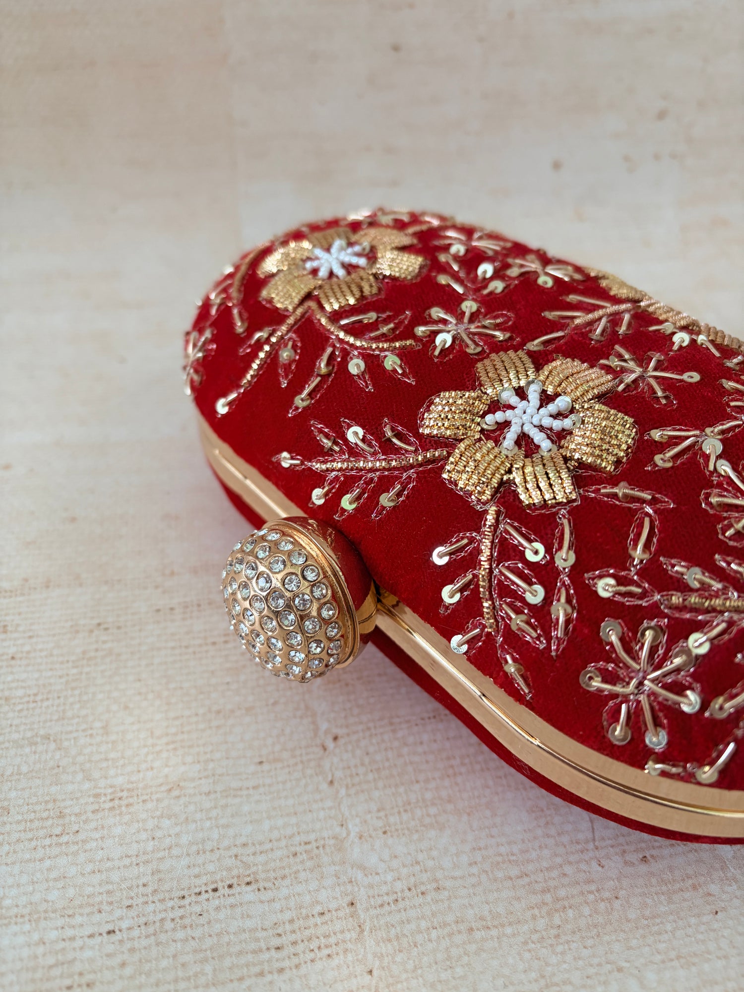 Red clutch with gold and white floral embroidery on a beige fabric background