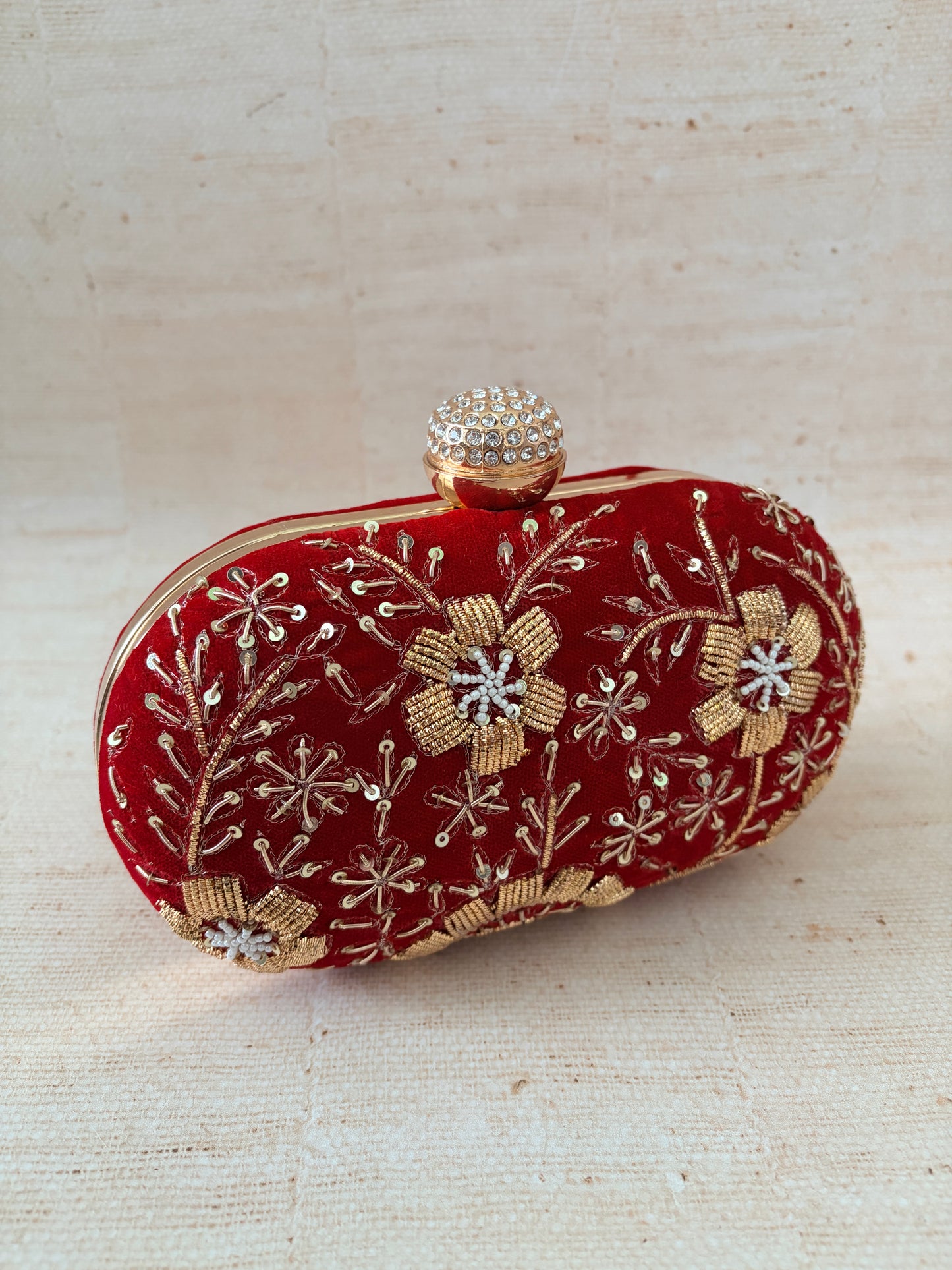 Red clutch with gold floral embroidery on a beige background
