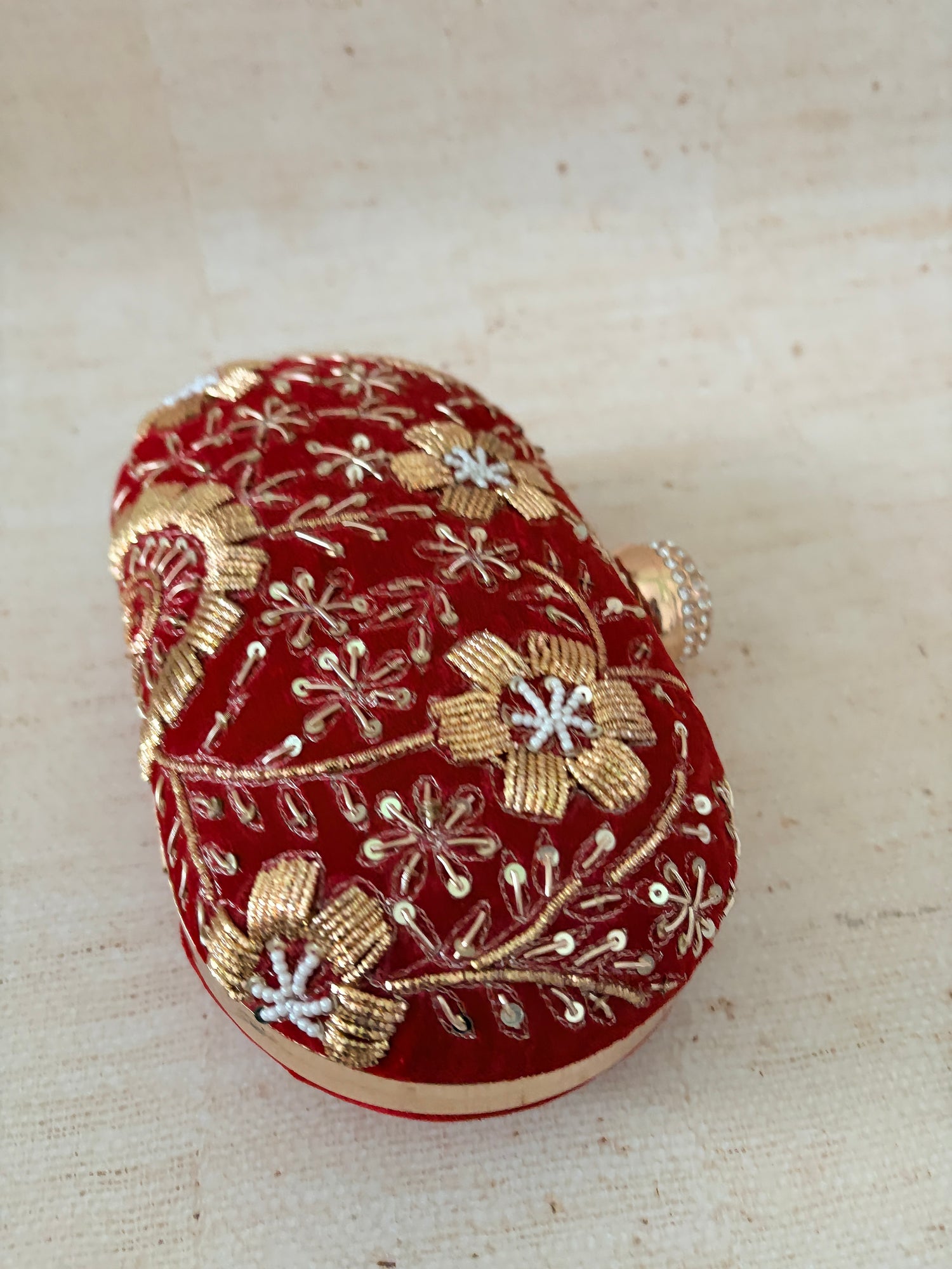 Red clutch bag with gold floral embroidery on a beige background