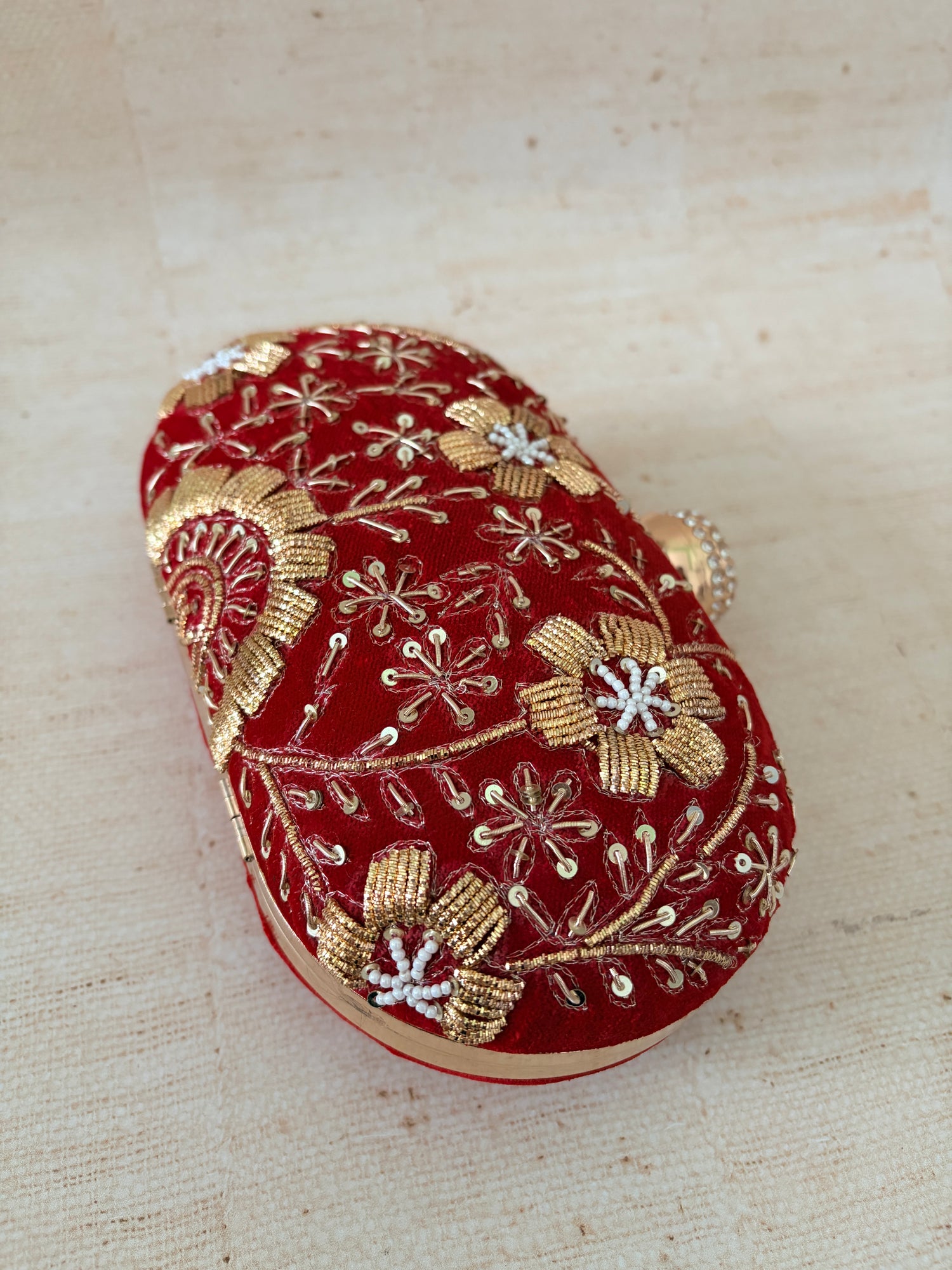 Red clutch with gold floral embroidery on a beige fabric background