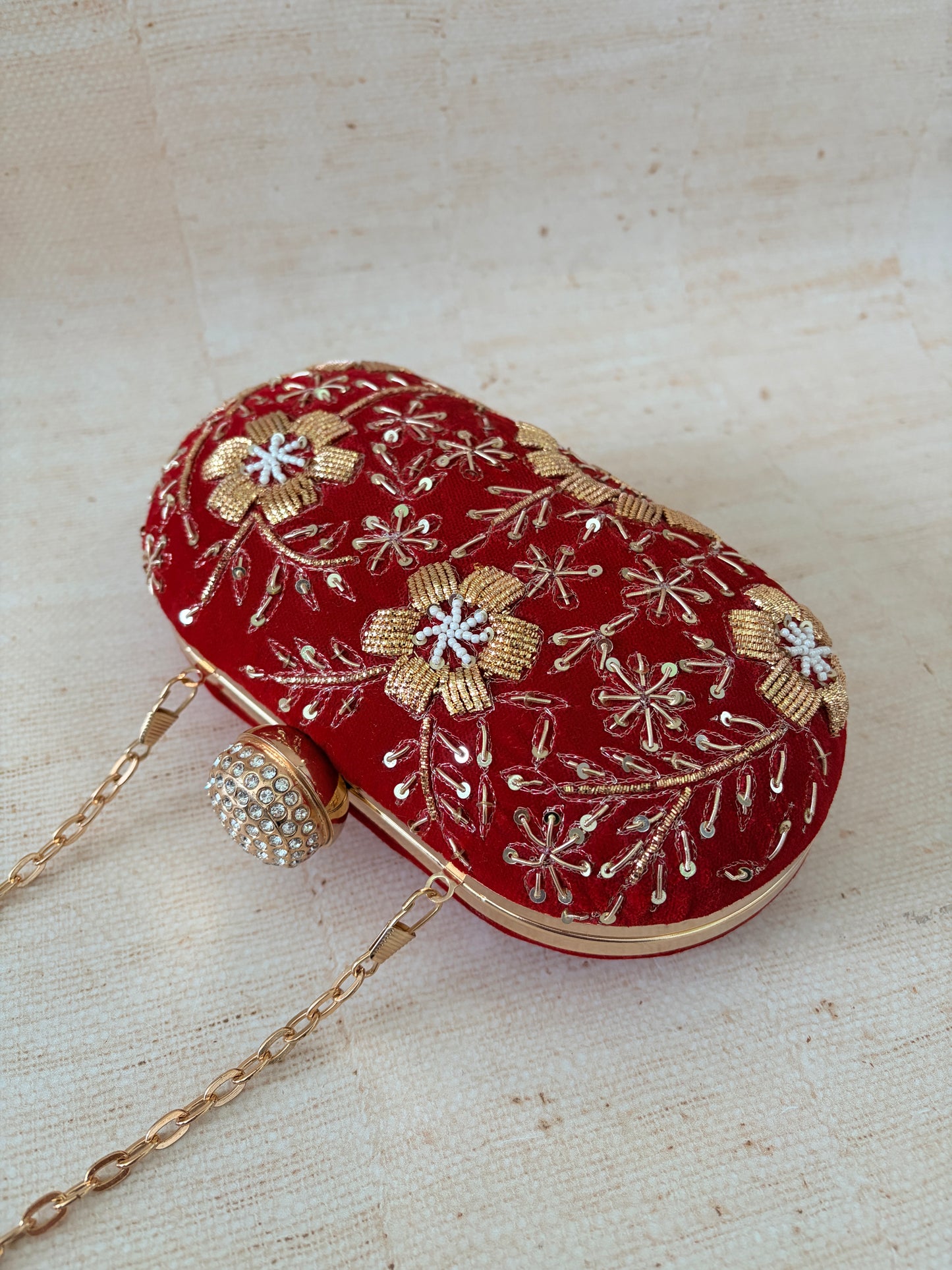 Red handbag with gold floral embroidery on a textured beige background