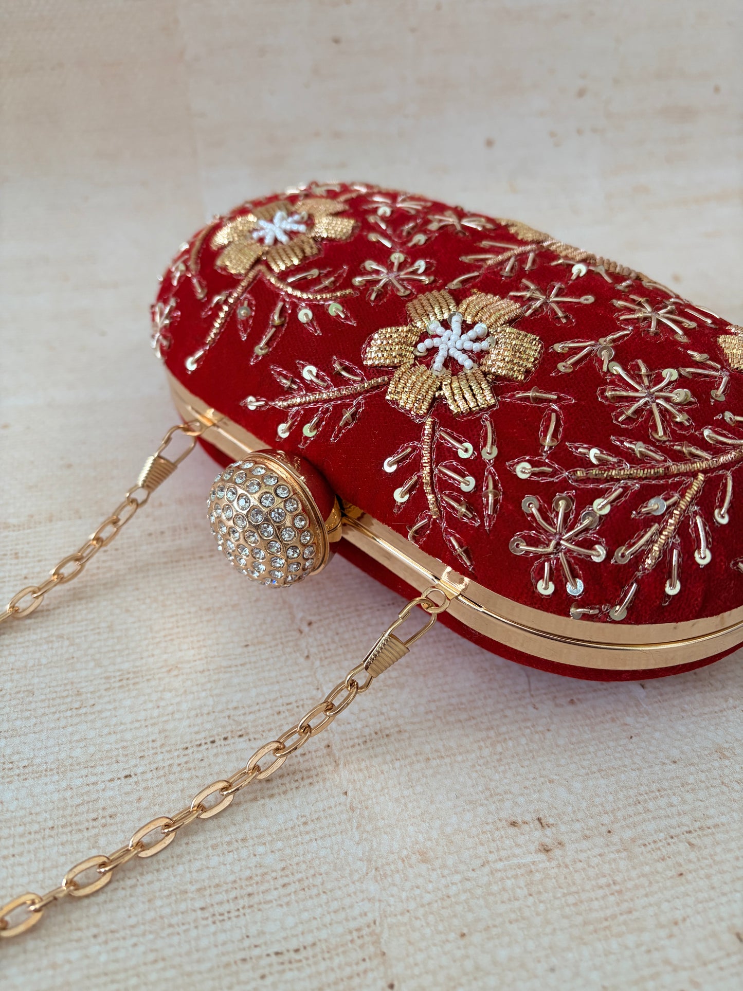 Red handbag with gold chain strap and floral embroidery on a beige background