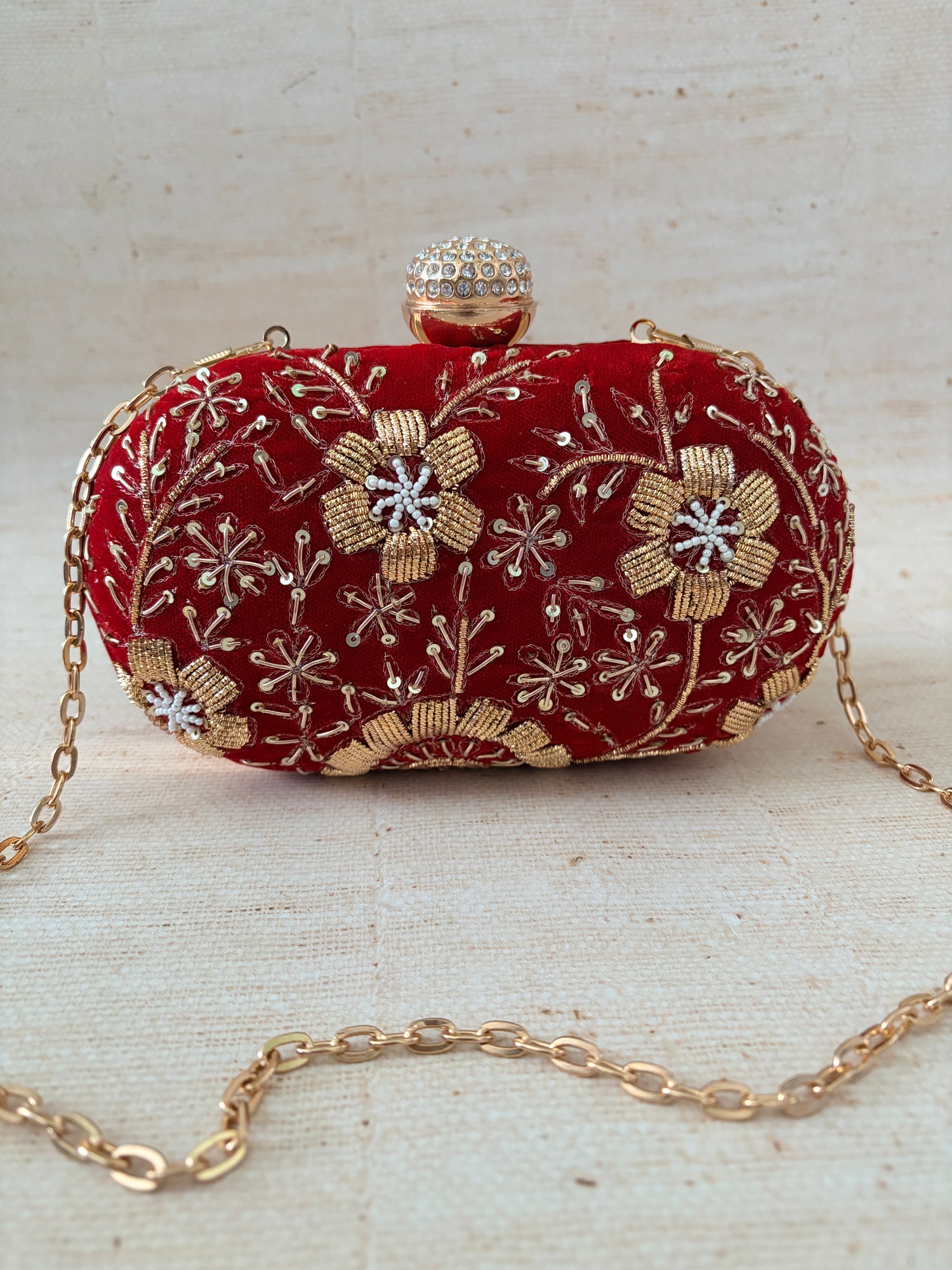 Red embroidered clutch with gold chain on a textured beige background