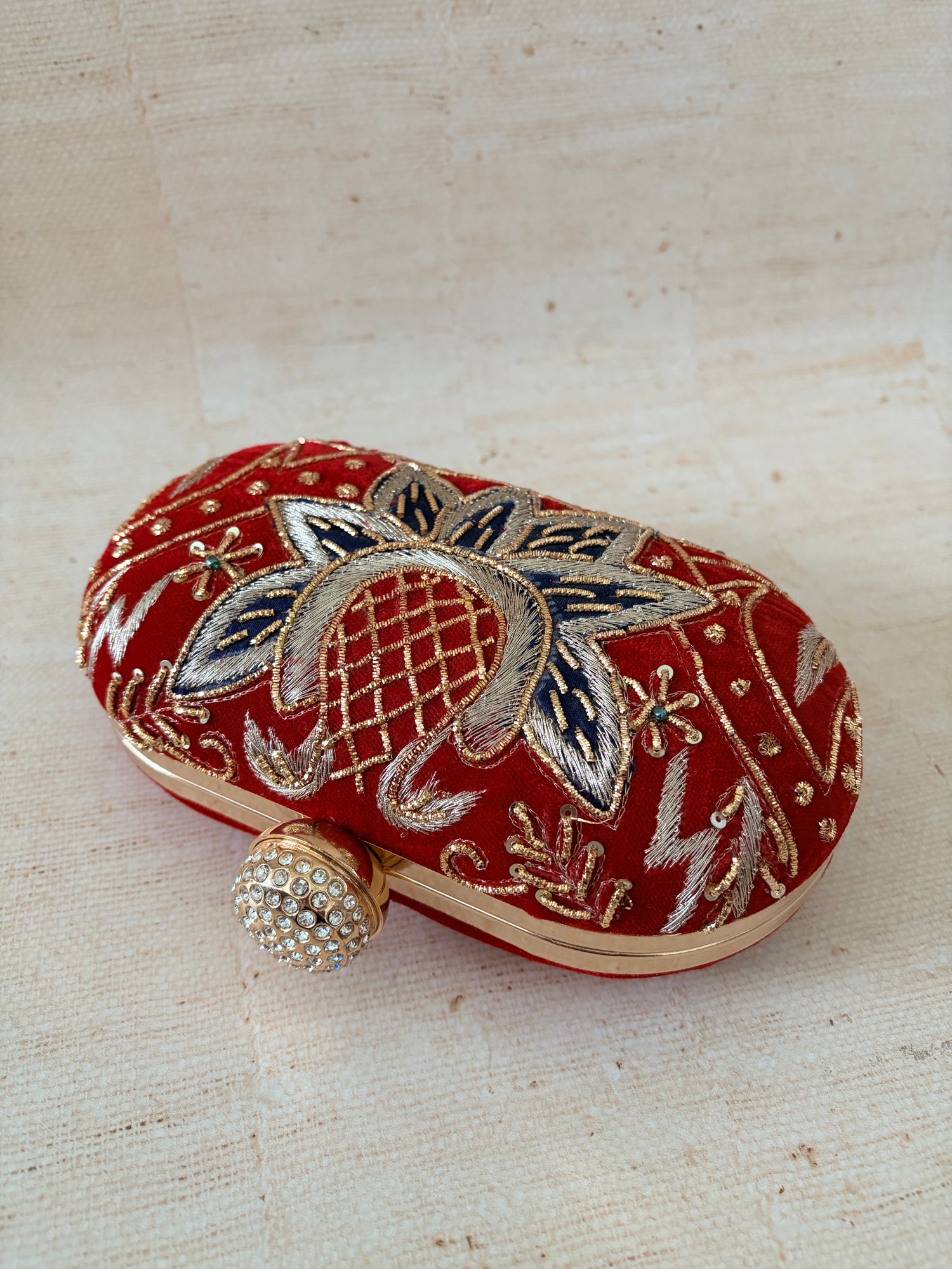 Decorative red clutch with gold and silver embroidery on a textured beige background