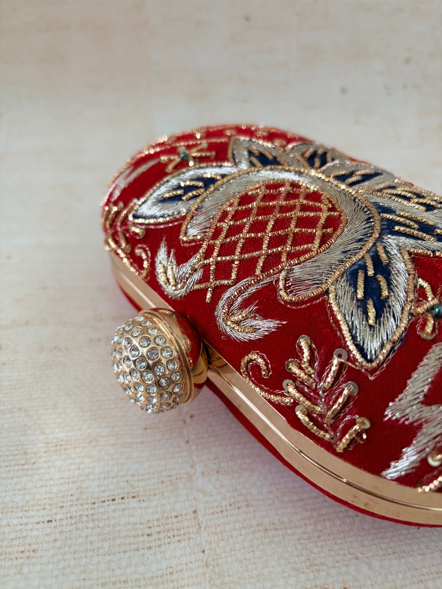 Decorative red pouch with intricate gold and blue embroidery on a textured beige background