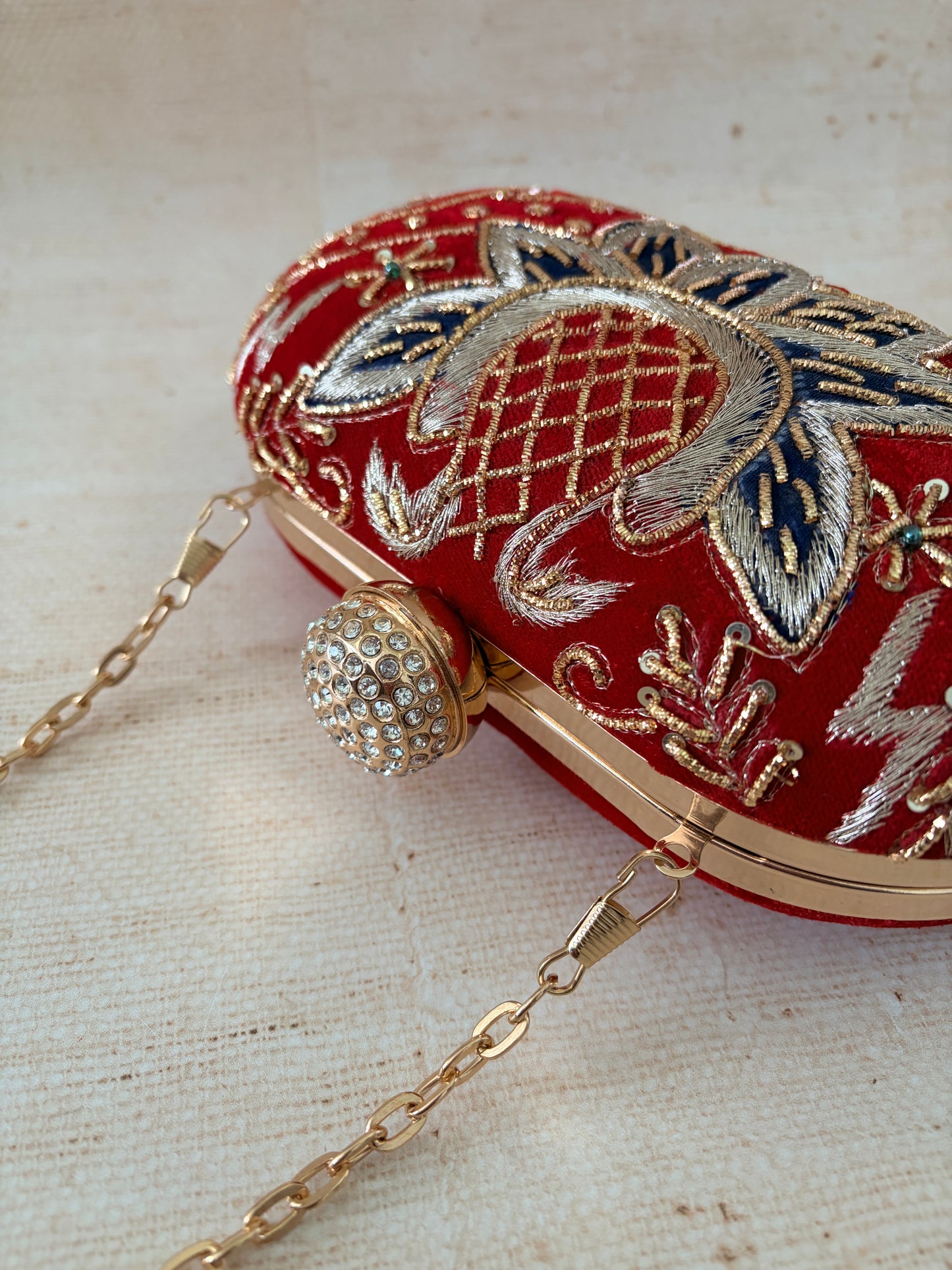 Decorative handbag with intricate embroidery and a chain strap on a textured fabric background