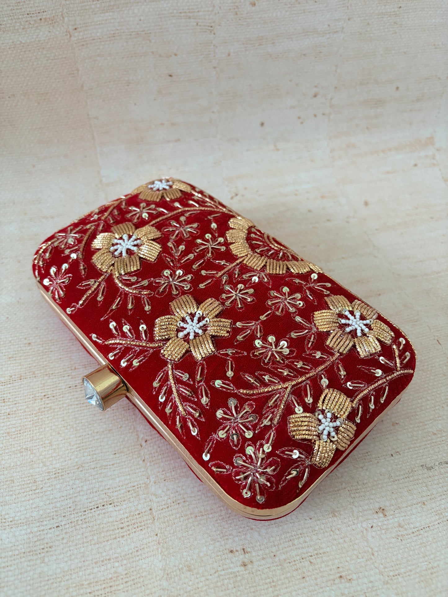 Red clutch with gold floral embroidery on a beige fabric background