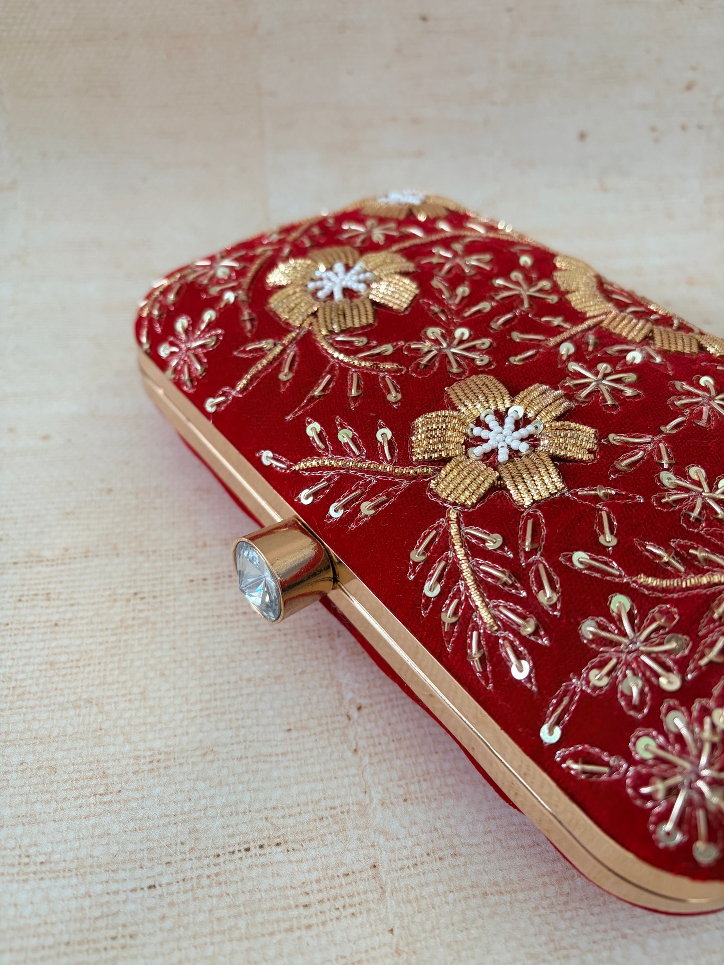 Red clutch with gold floral embroidery on a beige fabric background